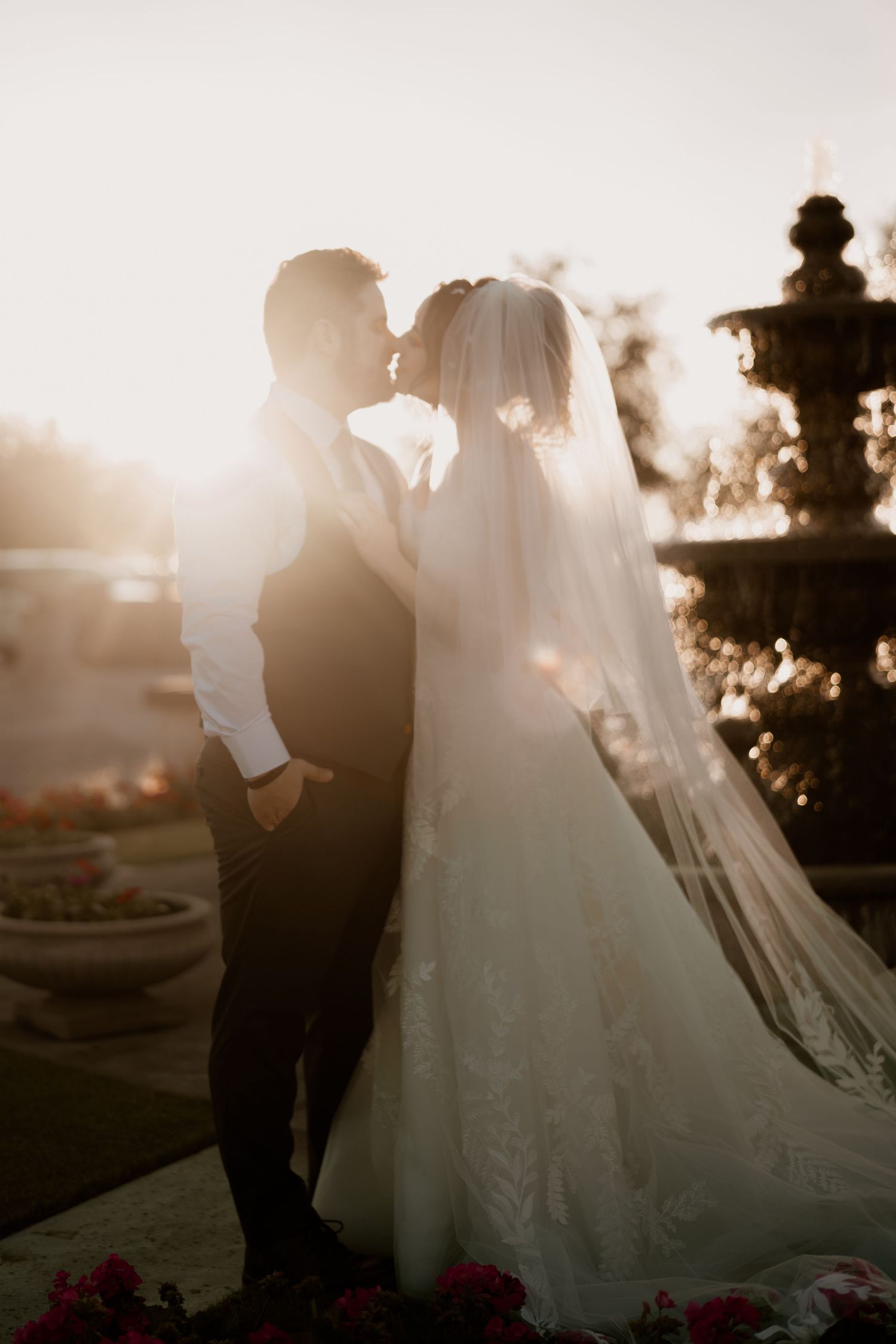 Silhouette of wedding couple embracing by fountain during golden hour.
