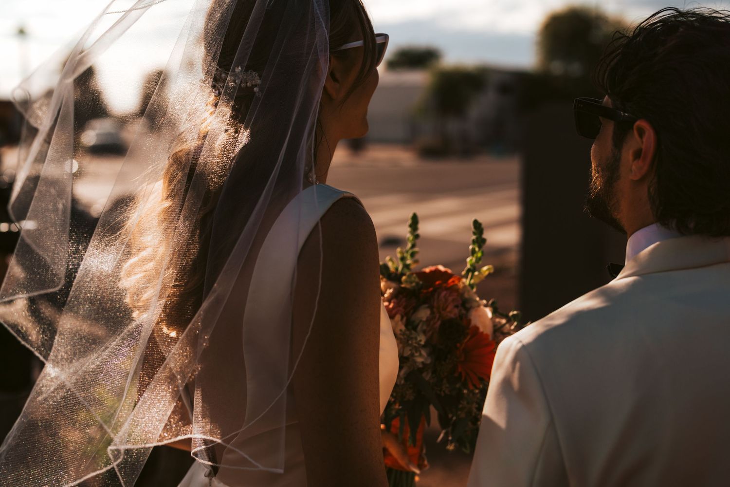 Backlit silhouette of wedding couple with flowing veil during sunset ceremony.