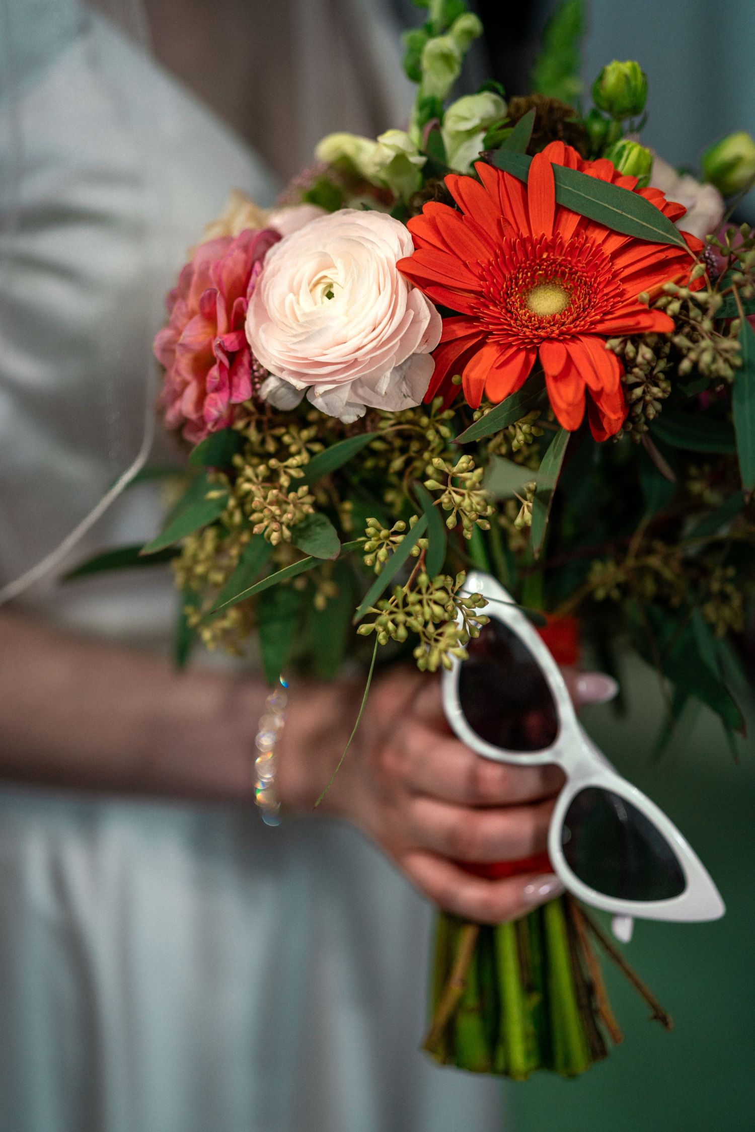 Bridal bouquet with red gerbera daisy and white ranunculus flowers with retro sunglasses.