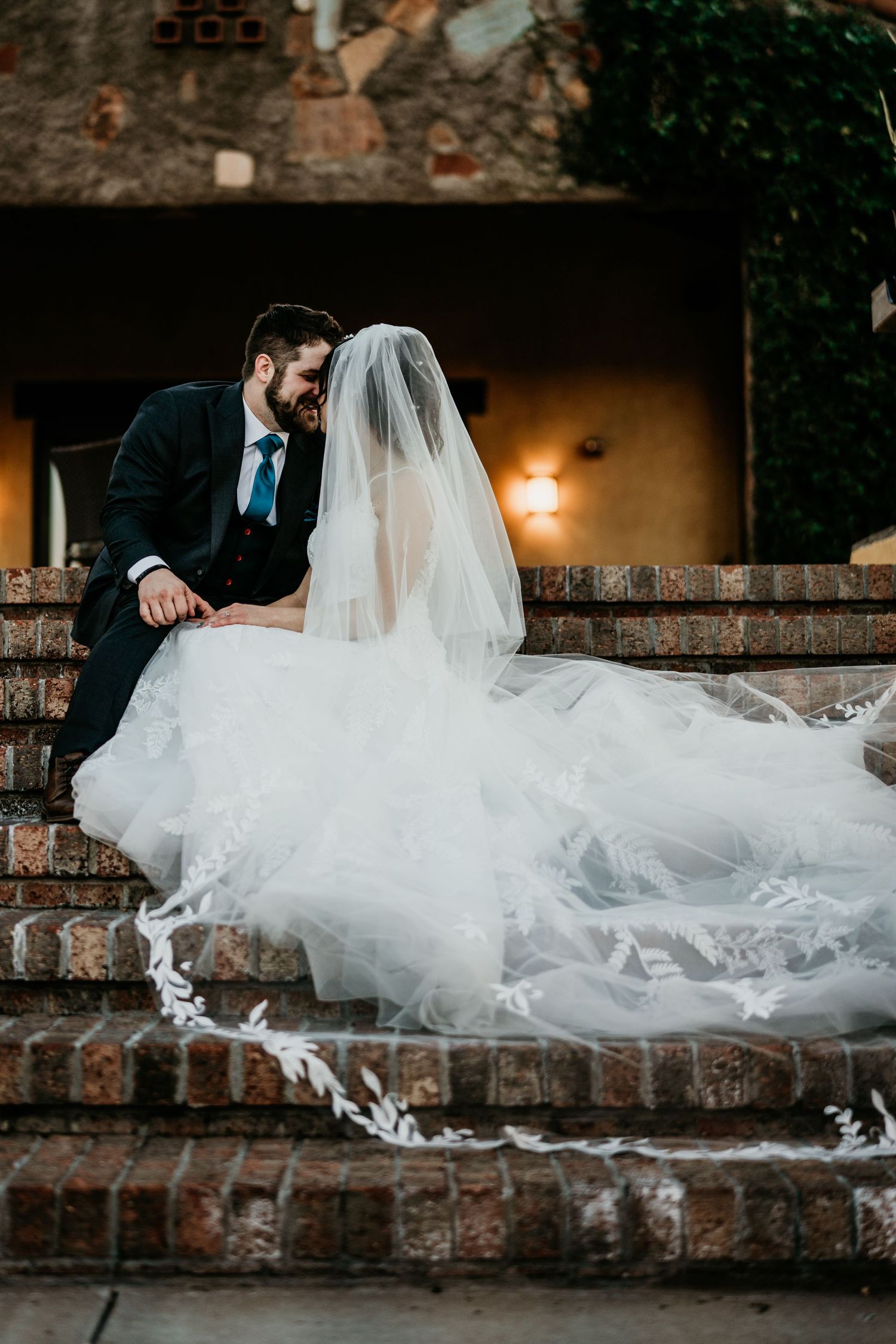 Wedding couple sitting on brick steps with flowing white veil cascading down.