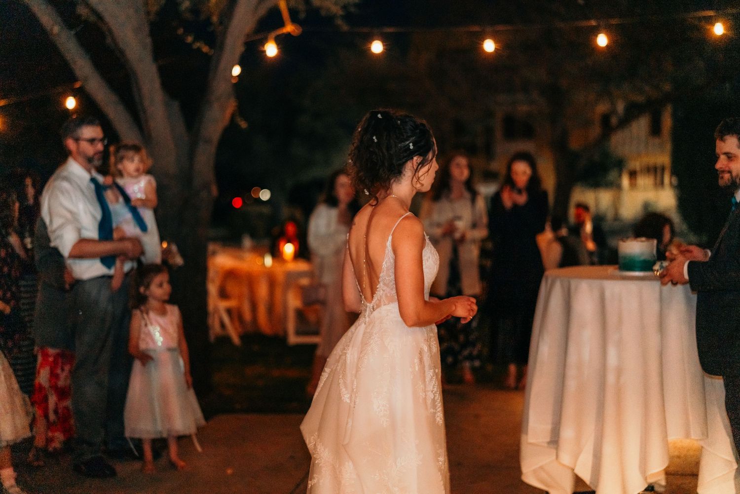 A backlit bride dances at her outdoor evening reception under string lights.