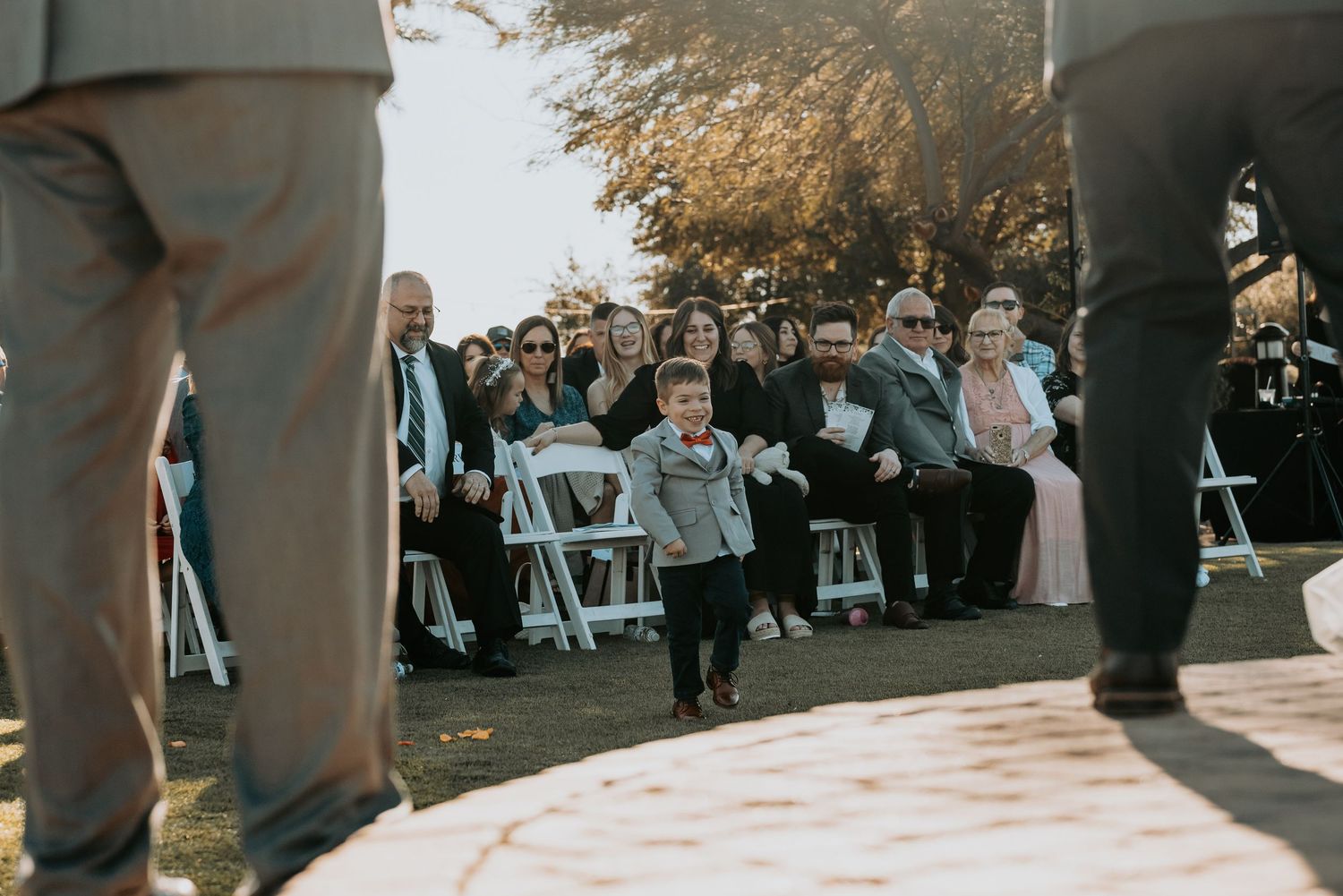 Young ring bearer walks down the aisle as wedding guests look on from white chairs.