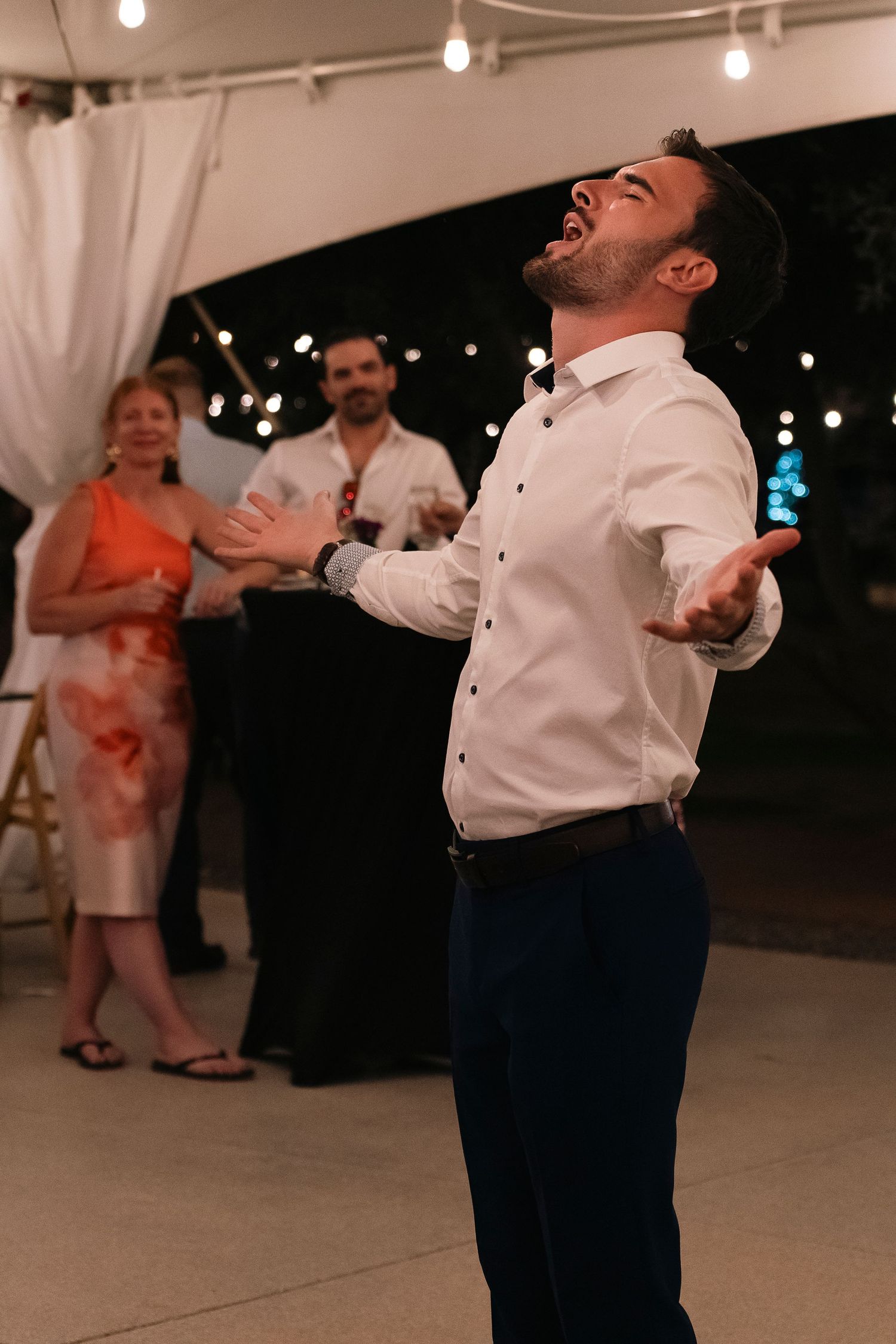 Person dancing joyfully at an indoor event with pendant lights and white curtains.