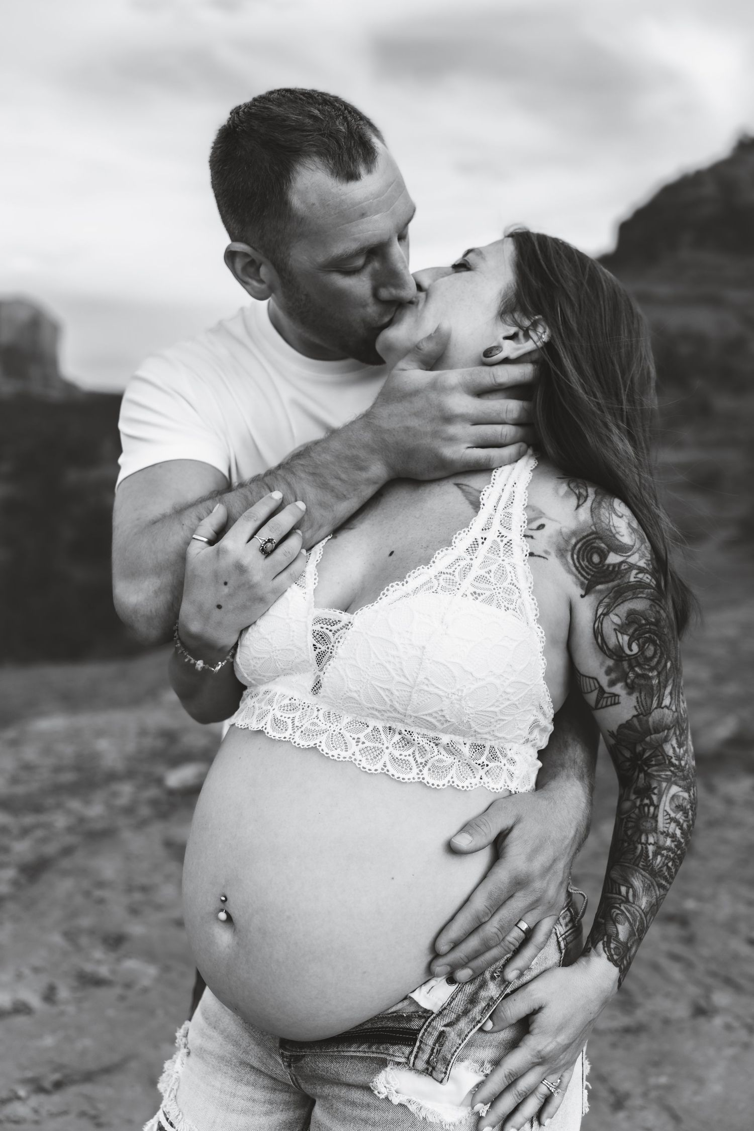 A black and white maternity photo shows an intimate moment between a couple outdoors, with the woman wearing lace.