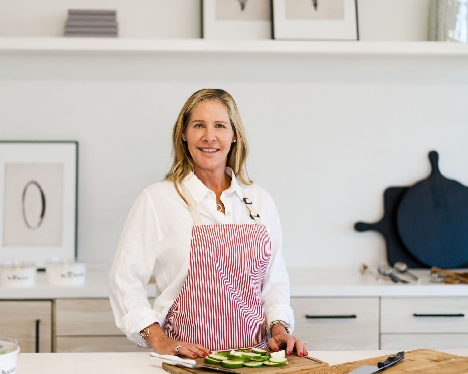 A person in a white shirt slices fresh vegetables on a wooden cutting board in a bright modern kitchen.