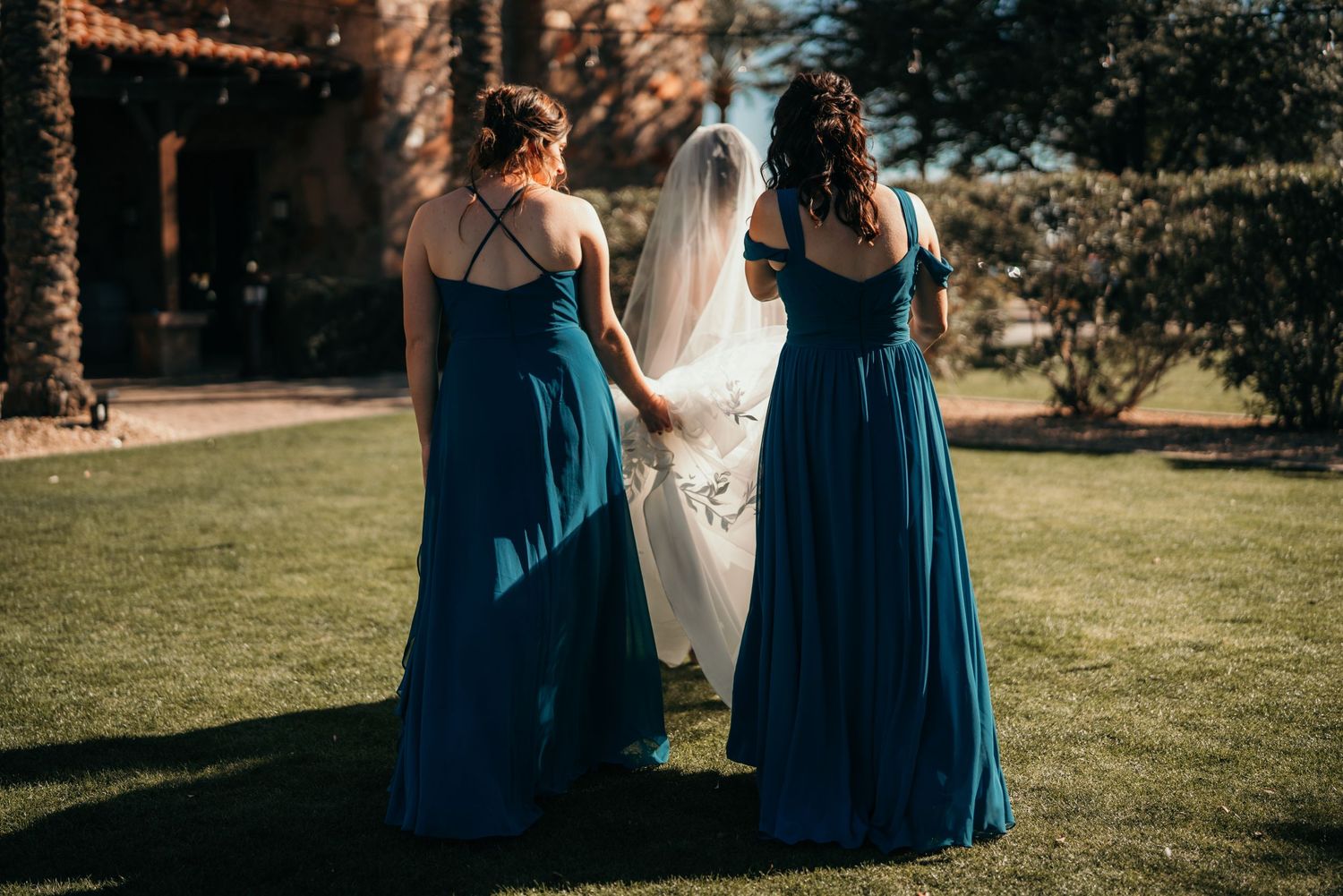Bridesmaids in teal blue dresses stand together during outdoor wedding ceremony.