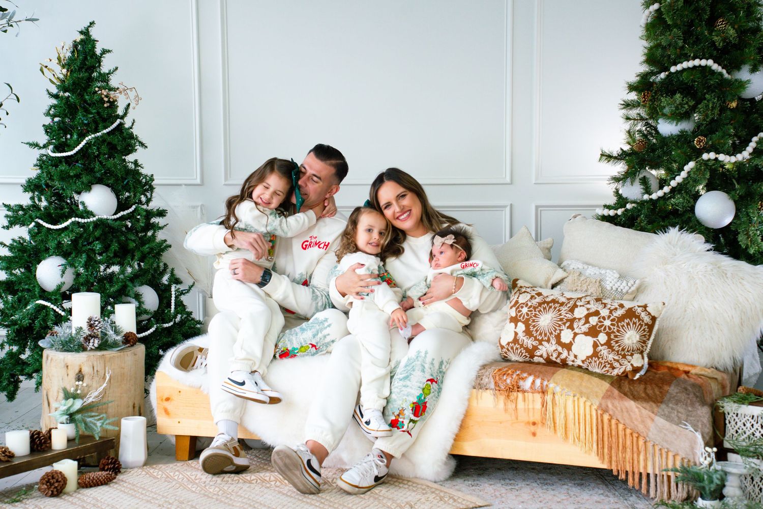 Family wearing matching white outfits relaxes together on a bed with Christmas decor in the background.
