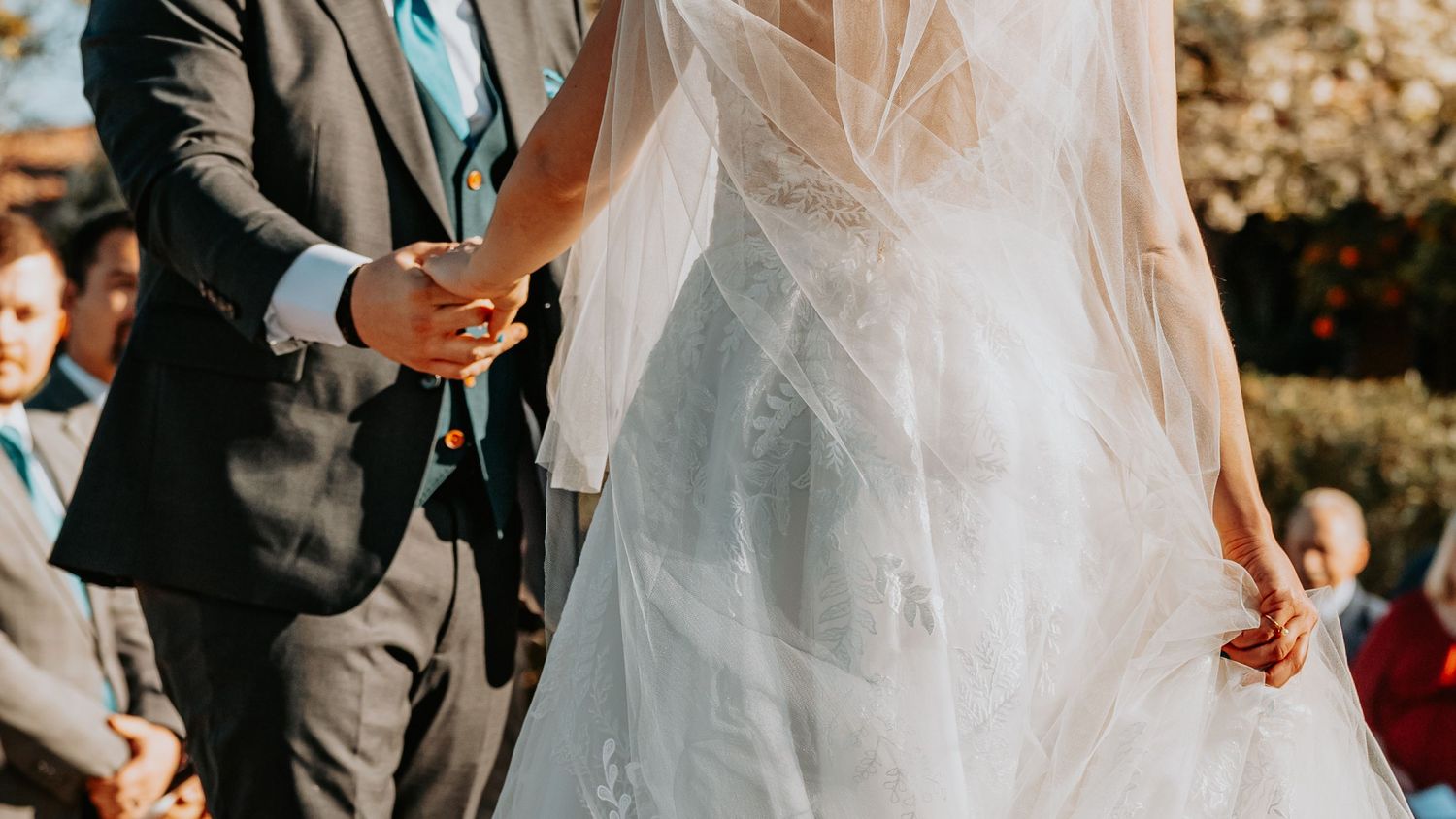 Partial view of couple during outdoor wedding ceremony with flowing veil detail.
