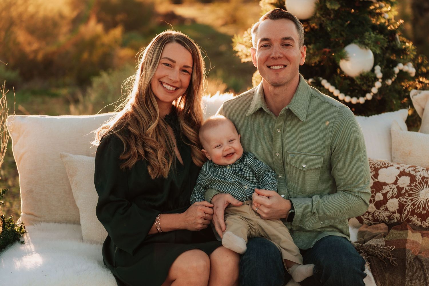 A family sits together outdoors during golden hour for a professional photo session in matching green and black outfits.