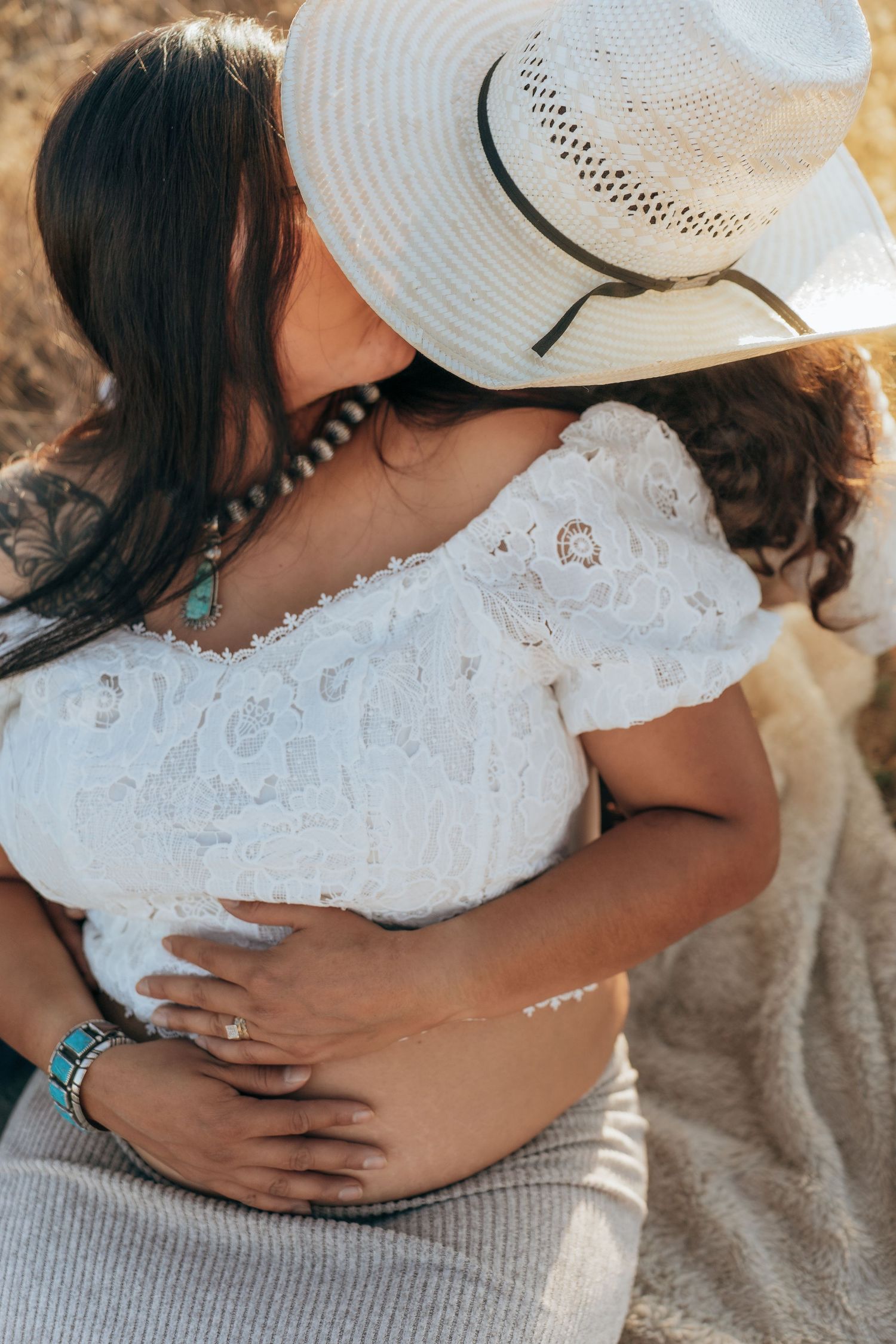 A series of intimate maternity photos showing hands cradling a pregnant belly while wearing a white lace top and cowboy hat.