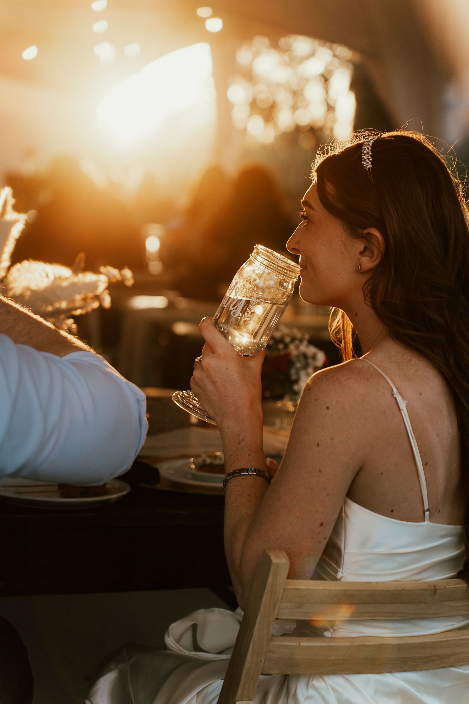 Person in white dress sips from a glass during golden hour.