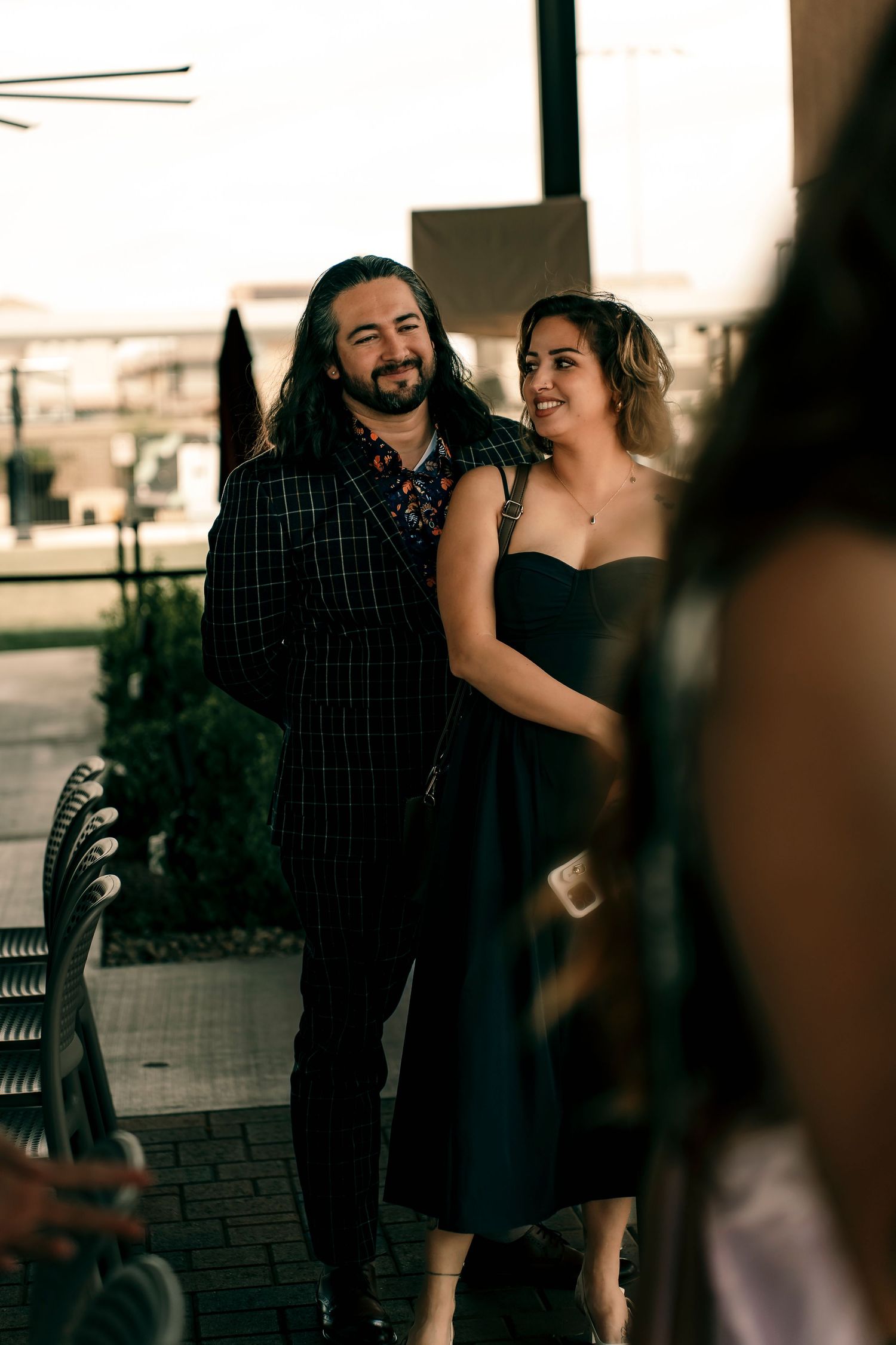 A couple shares an intimate moment outdoors, with the woman in a black dress and man in a plaid shirt.