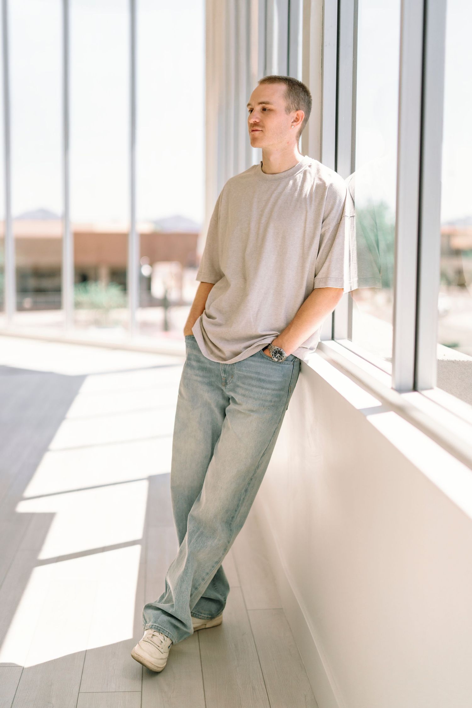 Casual portrait of someone in light clothing leaning against a bright window wall.