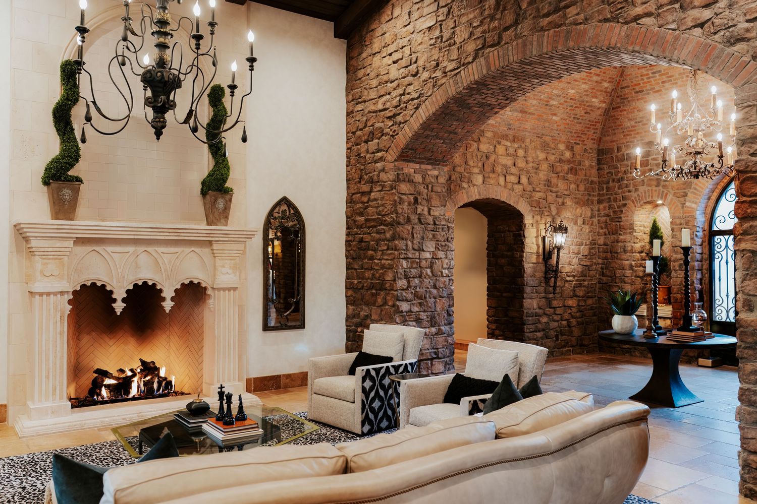 Interior view of a rustic stone castle corridor with elegant chandeliers and arched doorways.