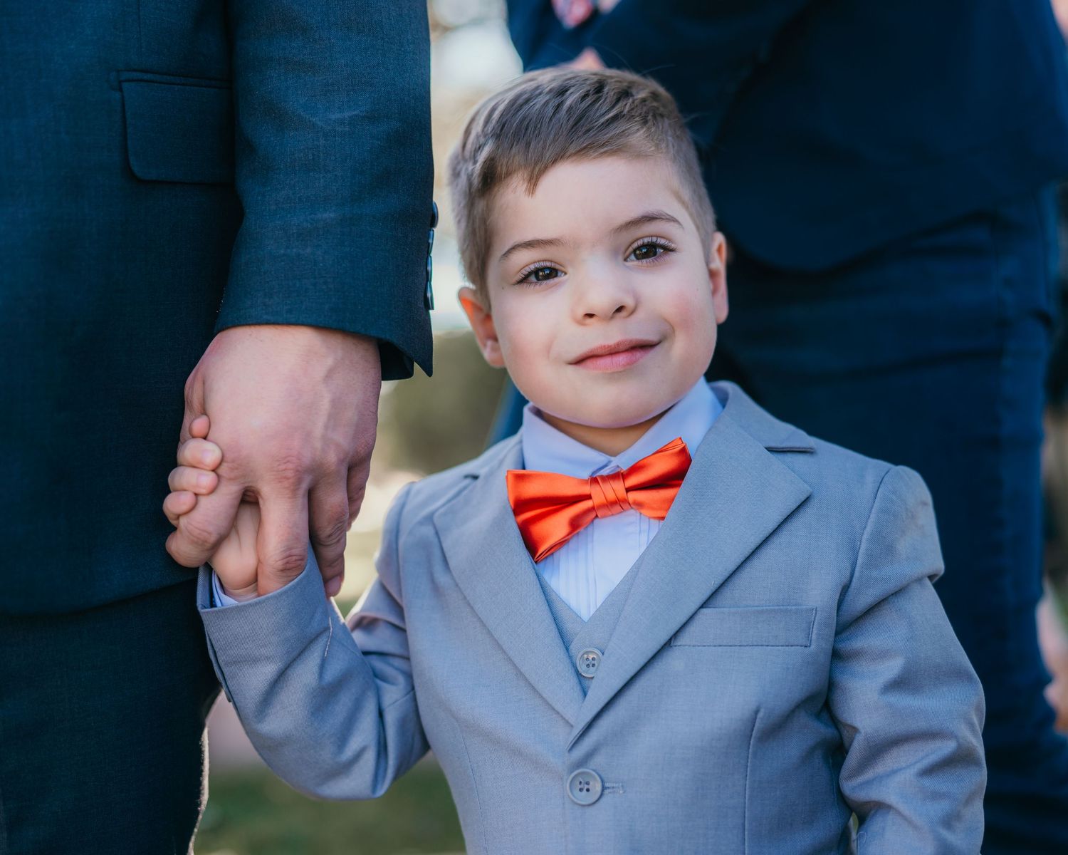 Young ring bearer in gray suit and orange bow tie at formal wedding event.
