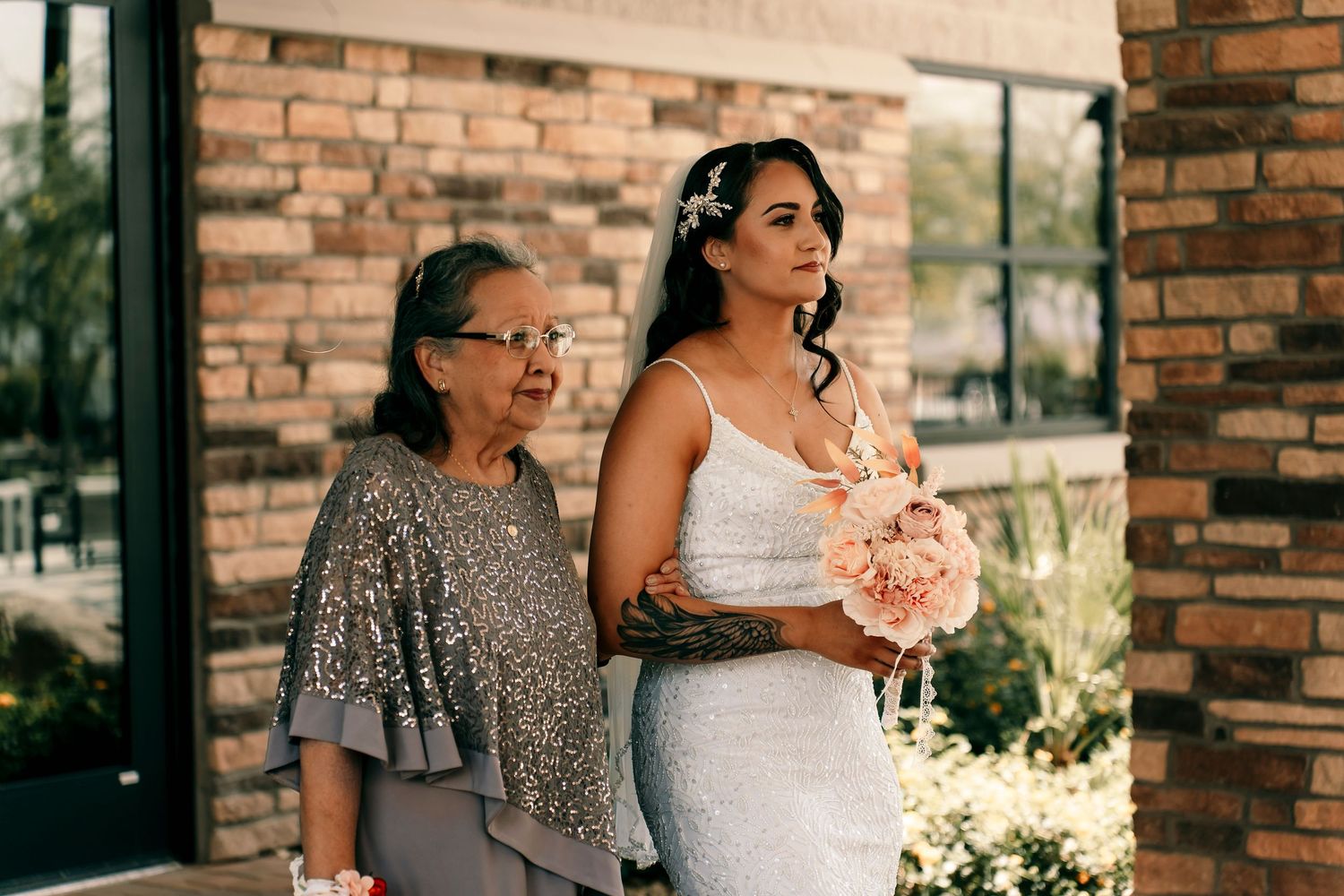 A bride in a white mermaid gown holds a bouquet while standing next to someone in a sequined dress.