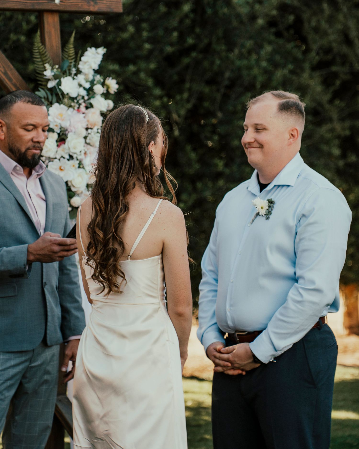 Wedding party members in light blue and gray attire gather outdoors during ceremony.