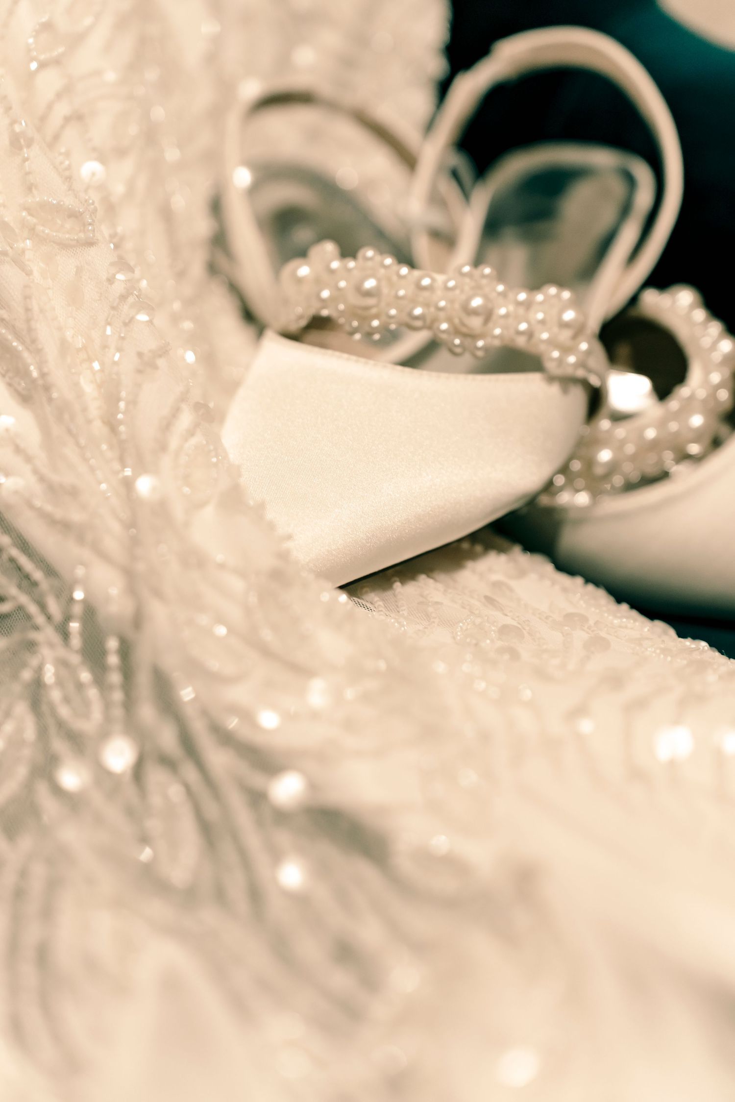 Wedding accessories including a pearl-adorned shoe against delicate lace fabric.