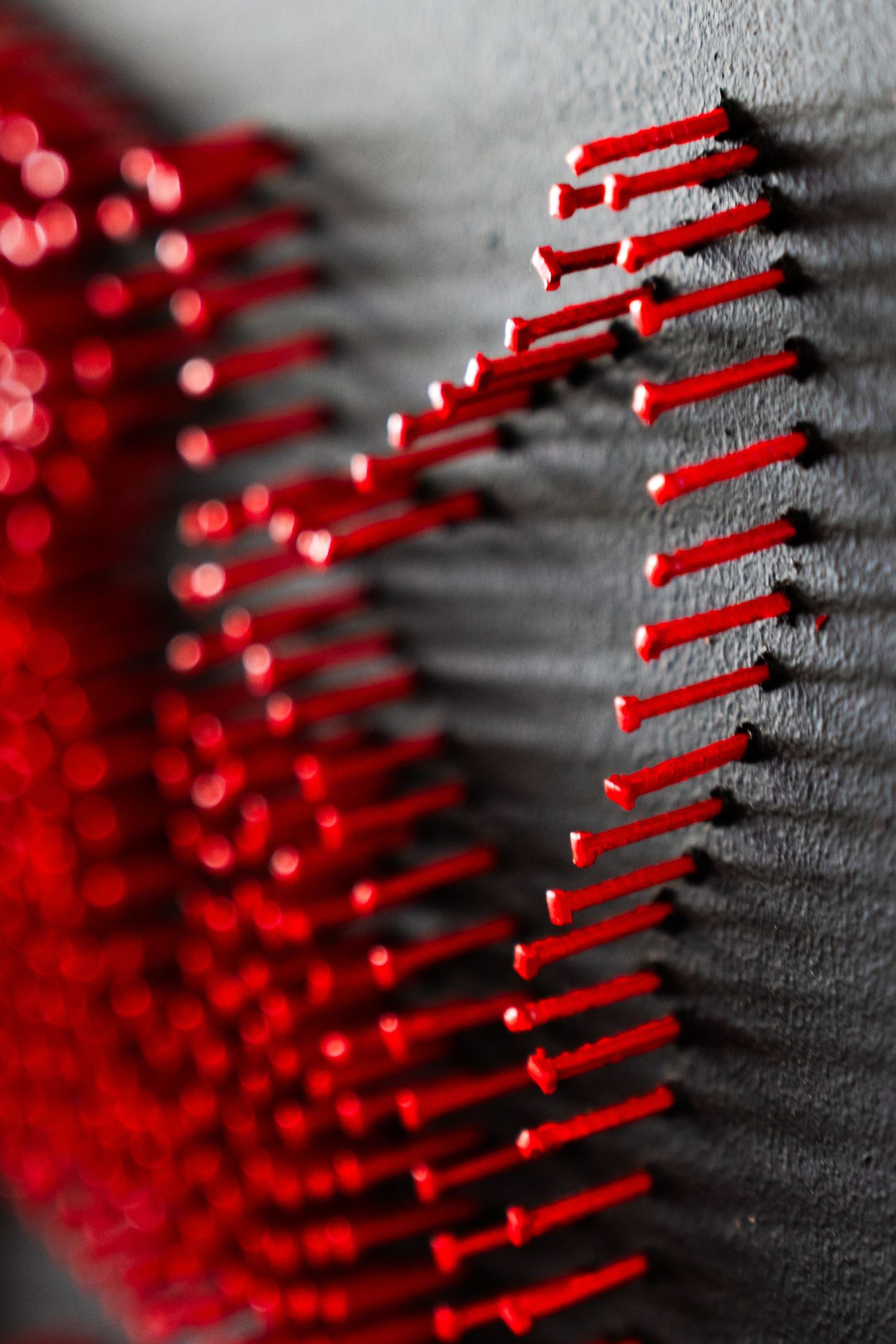 A series of red spiky lines arranged in a curved pattern against a gray background creates an abstract design effect.