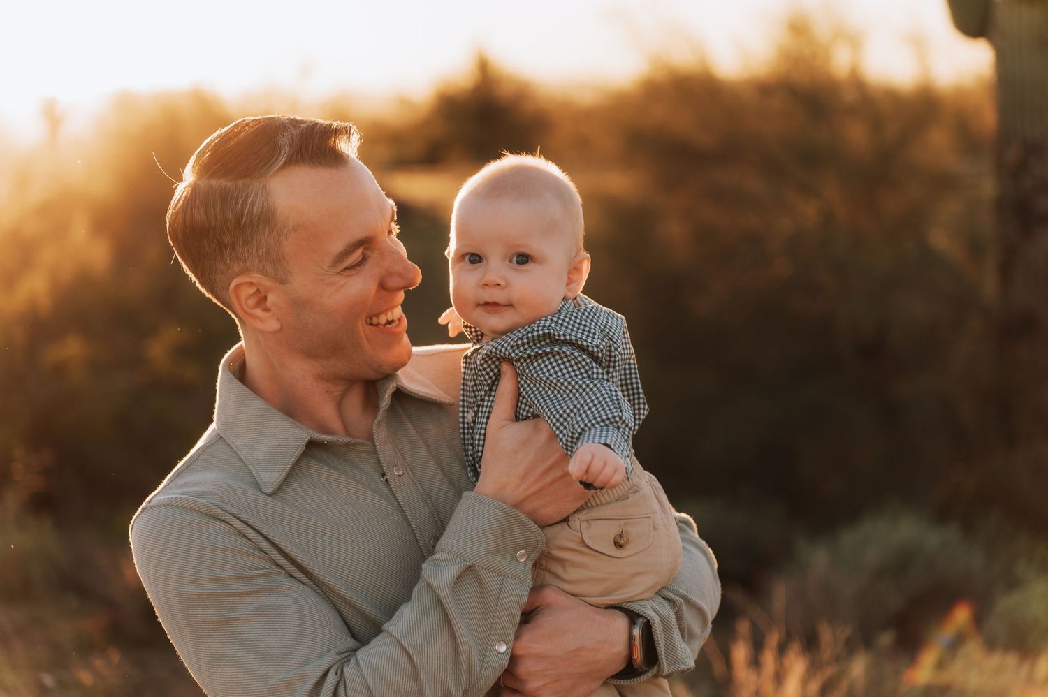 A parent and baby share joyful moments together in a golden sunset-lit field during an outdoor photo session.