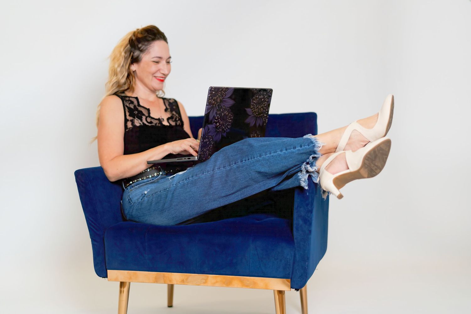 Person in jeans reclining on blue couch using laptop while working from home.