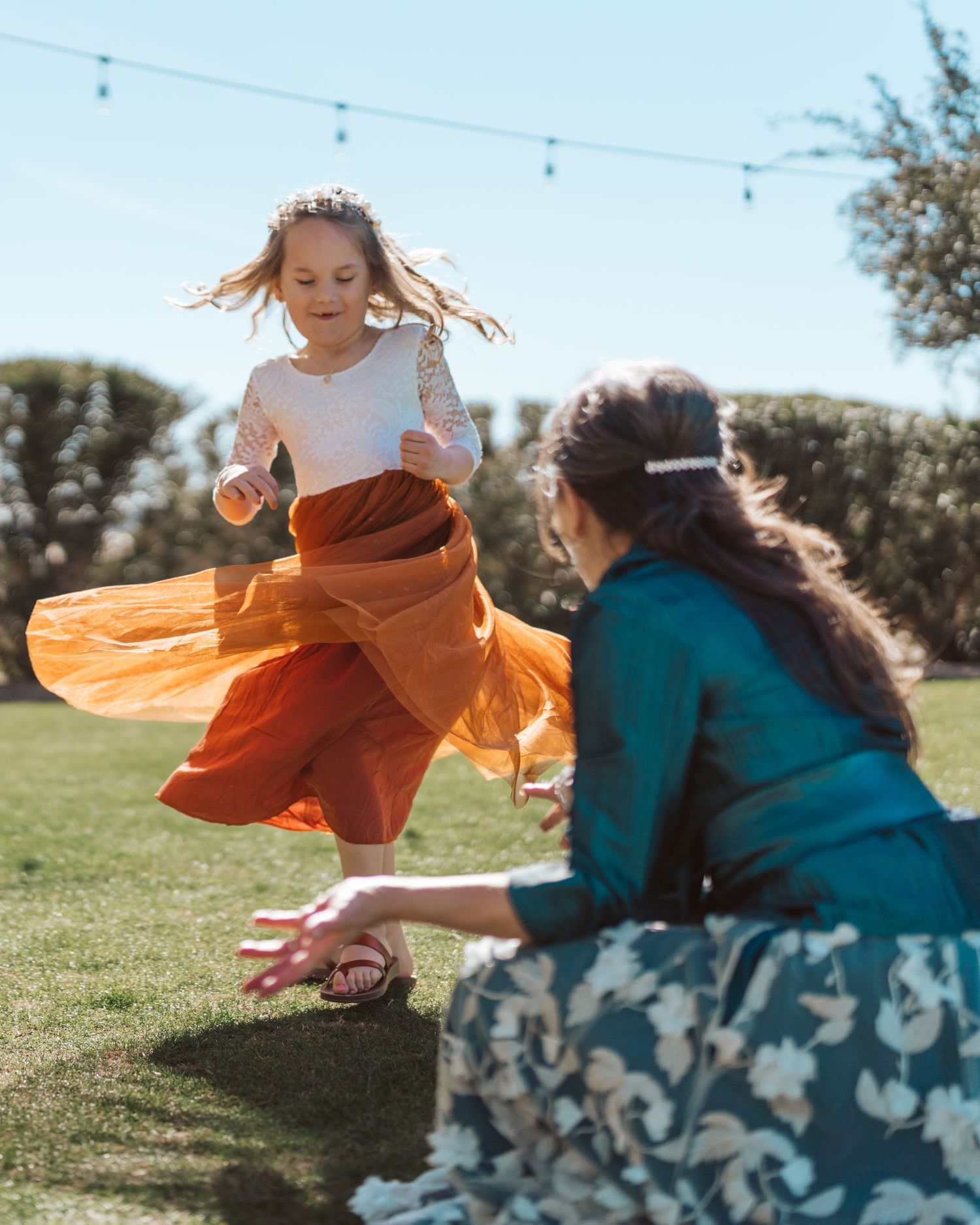Child in flowing orange dress playing on sunny grass field.