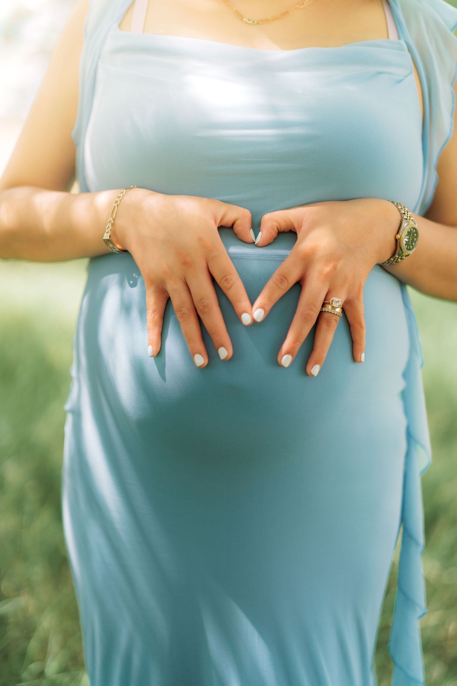 Hands forming heart shape over baby bump in light blue maternity dress.