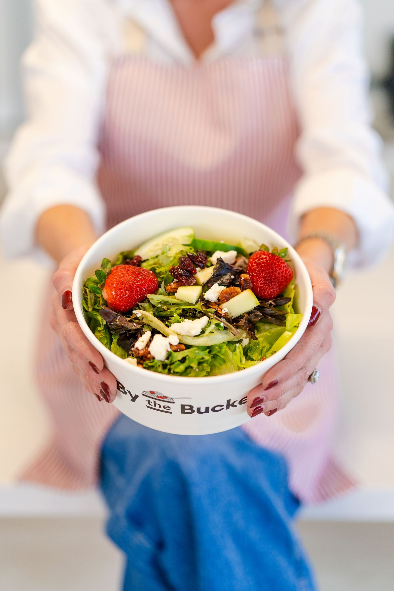 Hands holding a fresh salad bowl with strawberries, greens and other toppings in white ceramic dish.