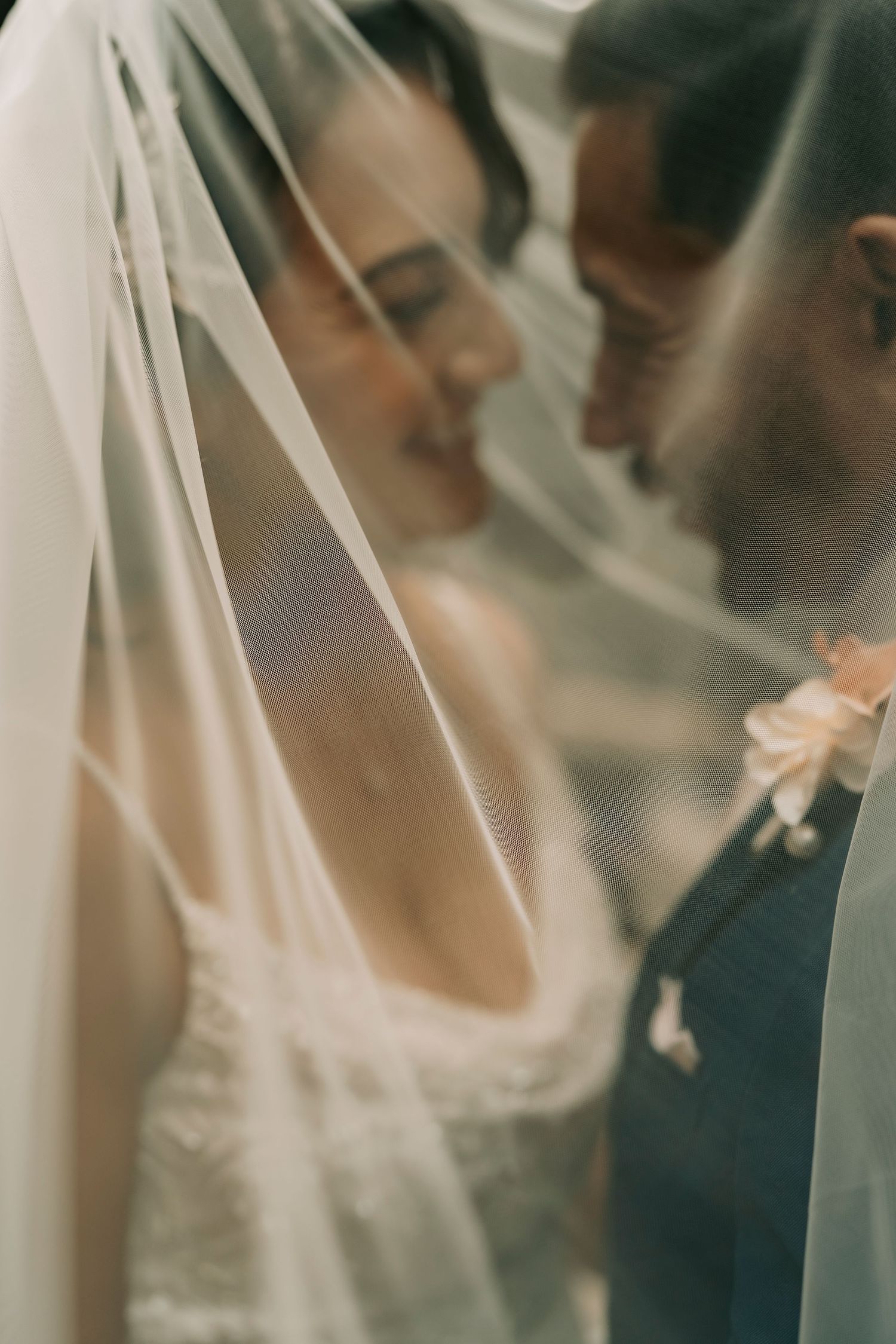 Romantic wedding portrait through delicate white veil showing bride and groom in an intimate moment.
