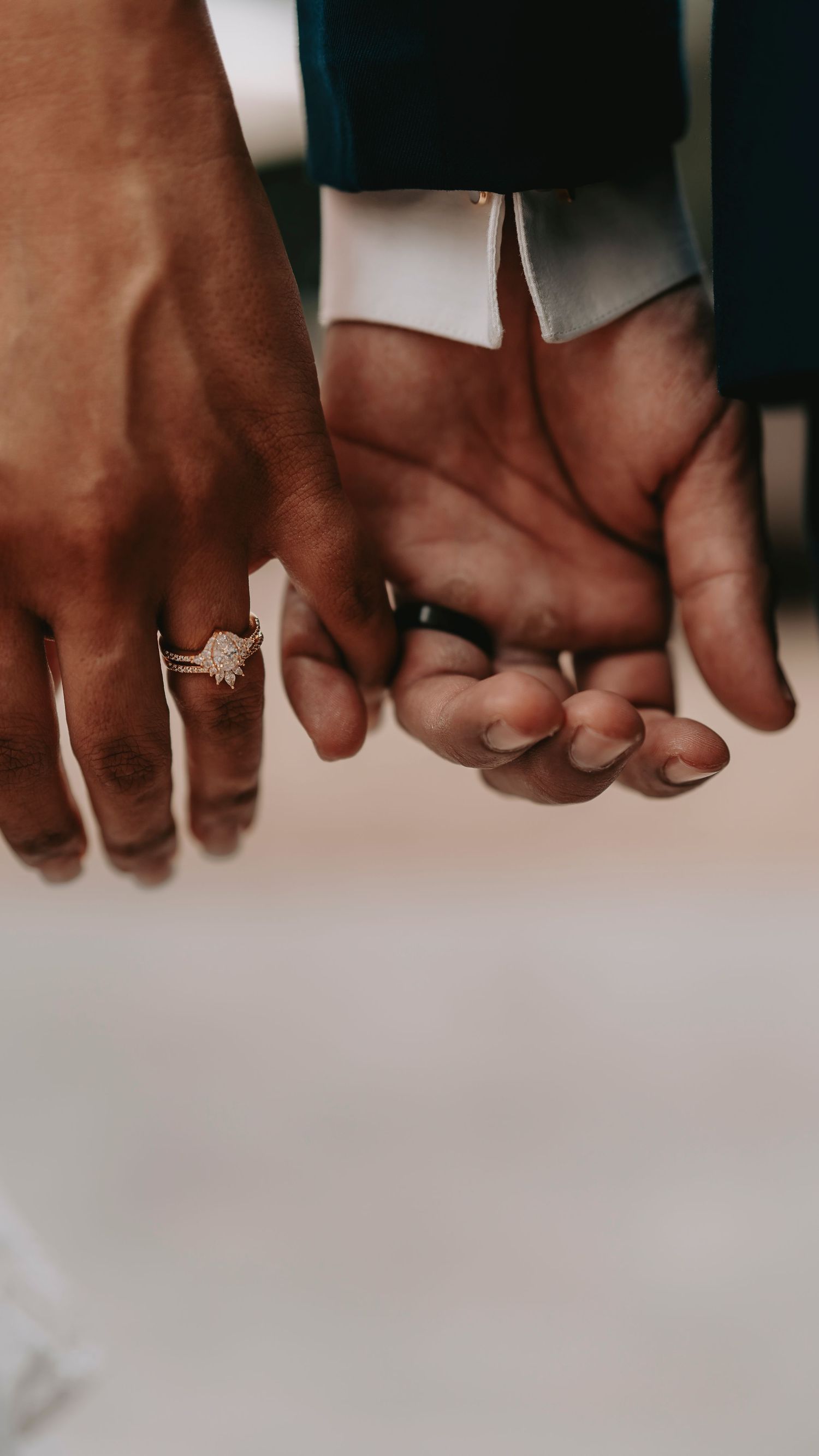 Close-up of two hands with wedding rings intertwined against light background.