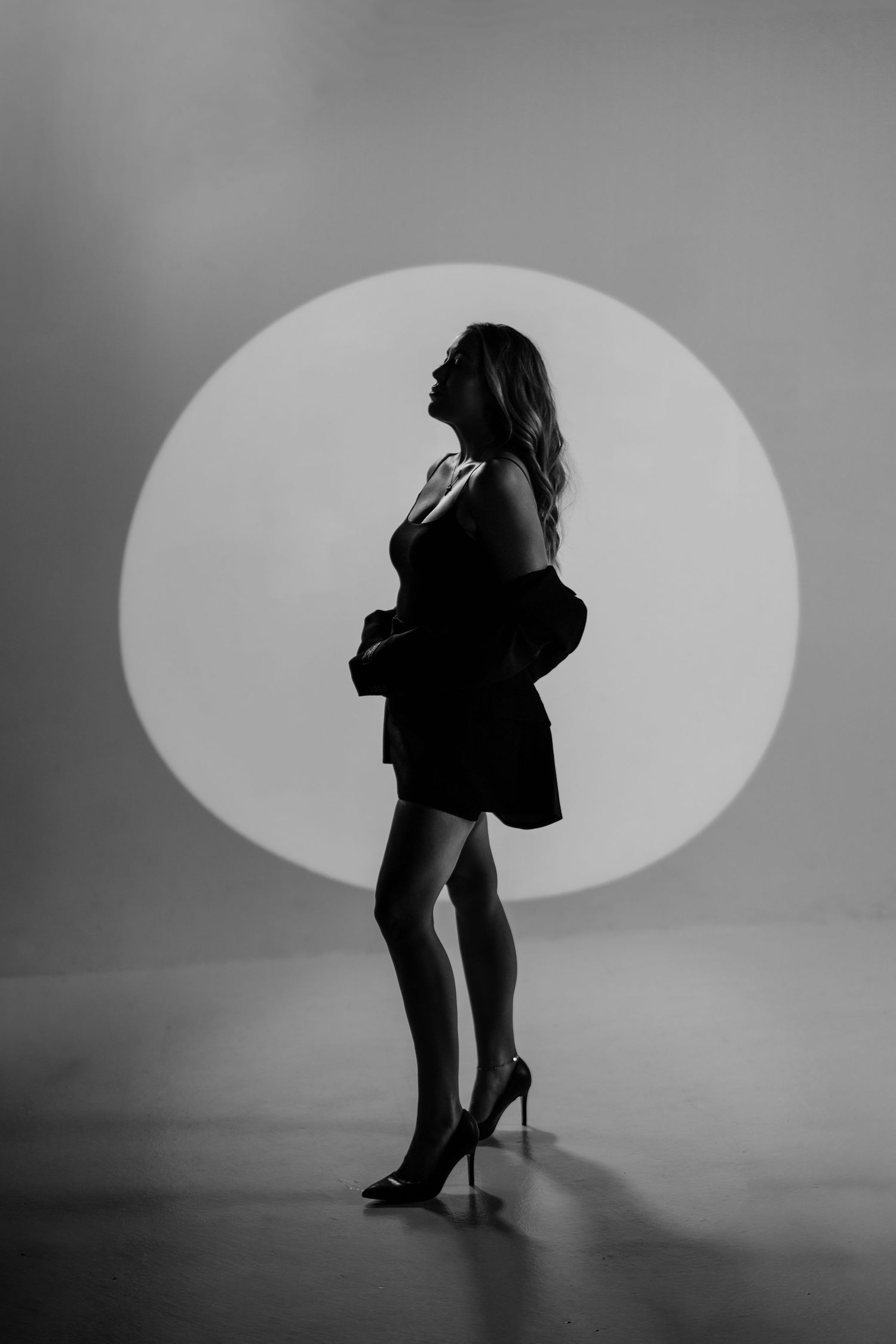 Dramatic black and white silhouette of a woman in heels against a circular light backdrop.