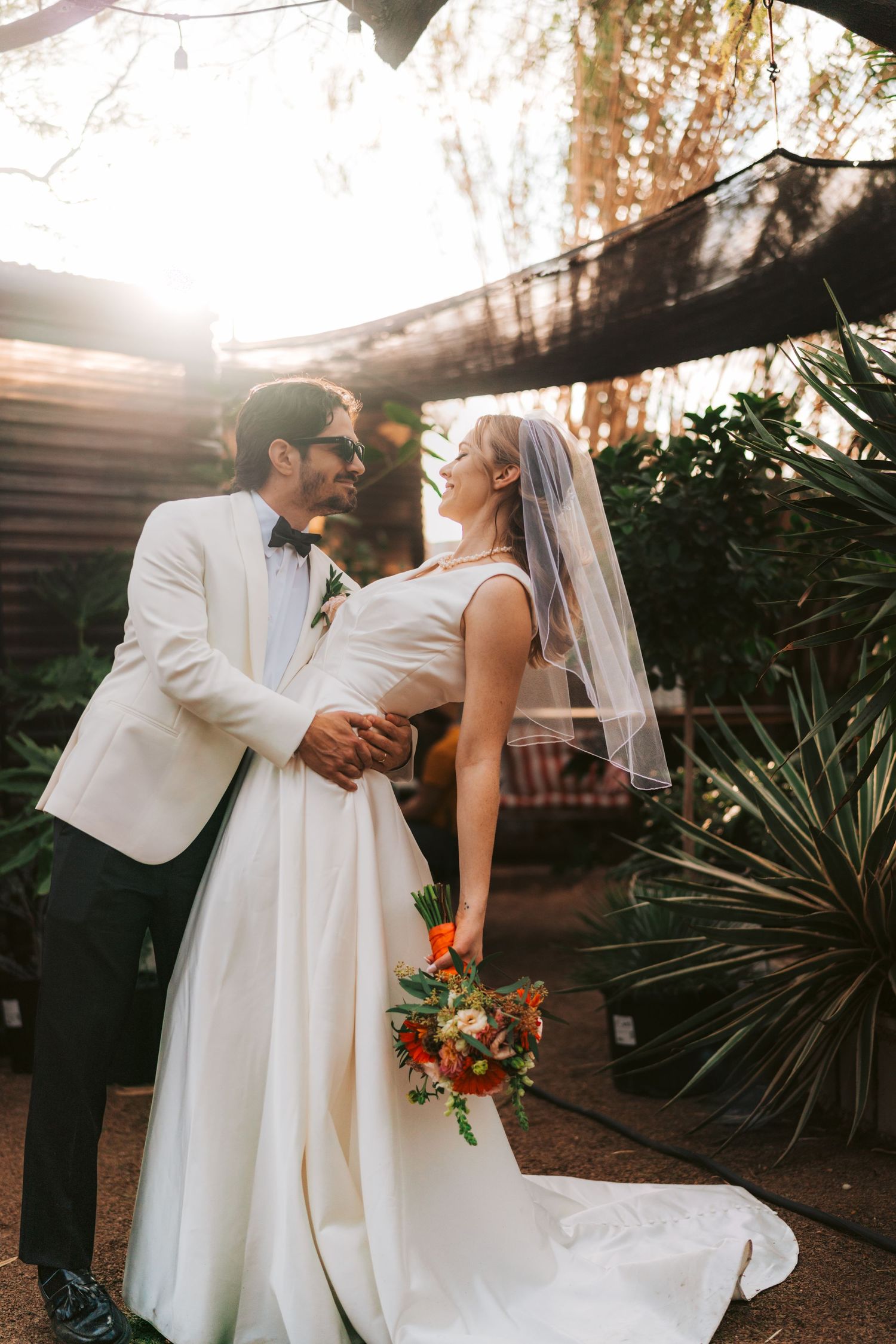 A playful wedding portrait in a garden setting with tropical plants.