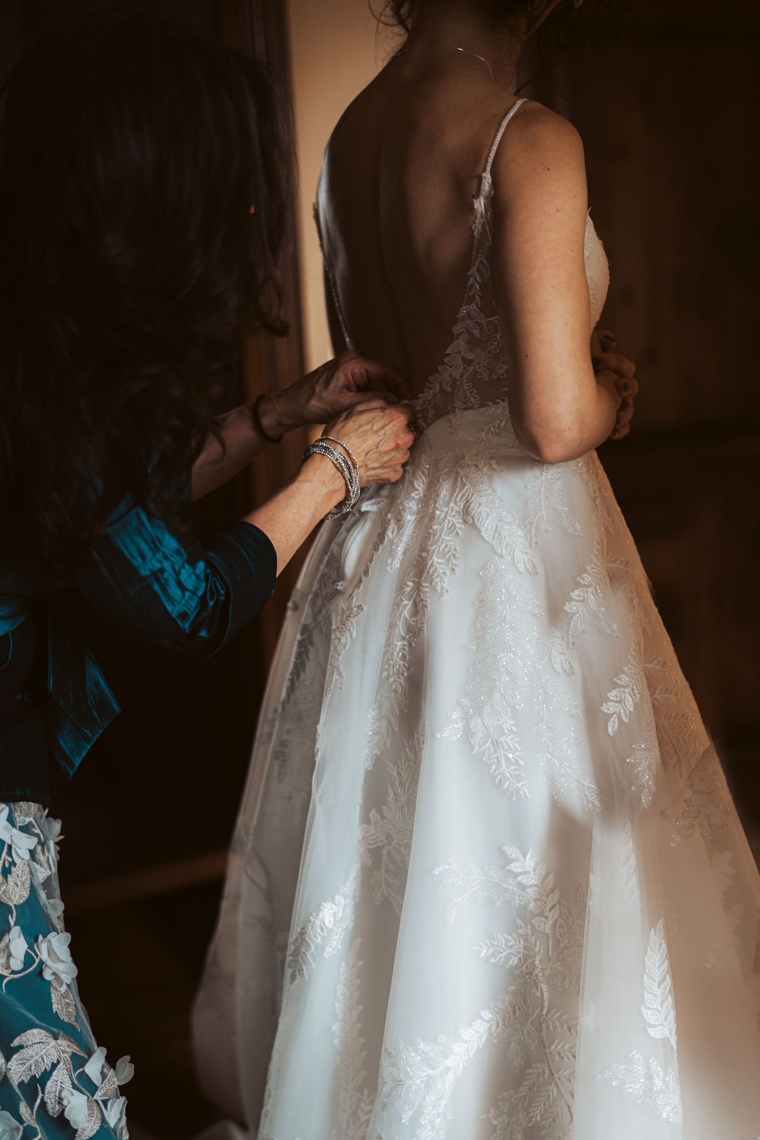 Close-up detail of lace wedding dress being adjusted from behind.