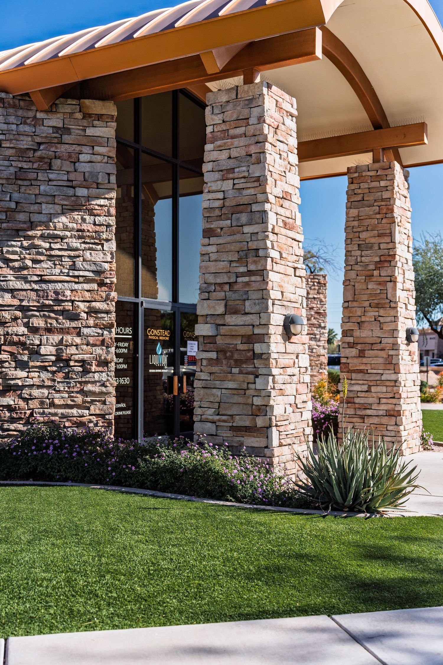Modern commercial building exterior with stone columns and landscaped lawn along a concrete walkway.