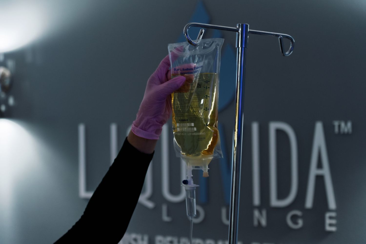 A hand lifts a glass of light beer against a dark background with illuminated signage.