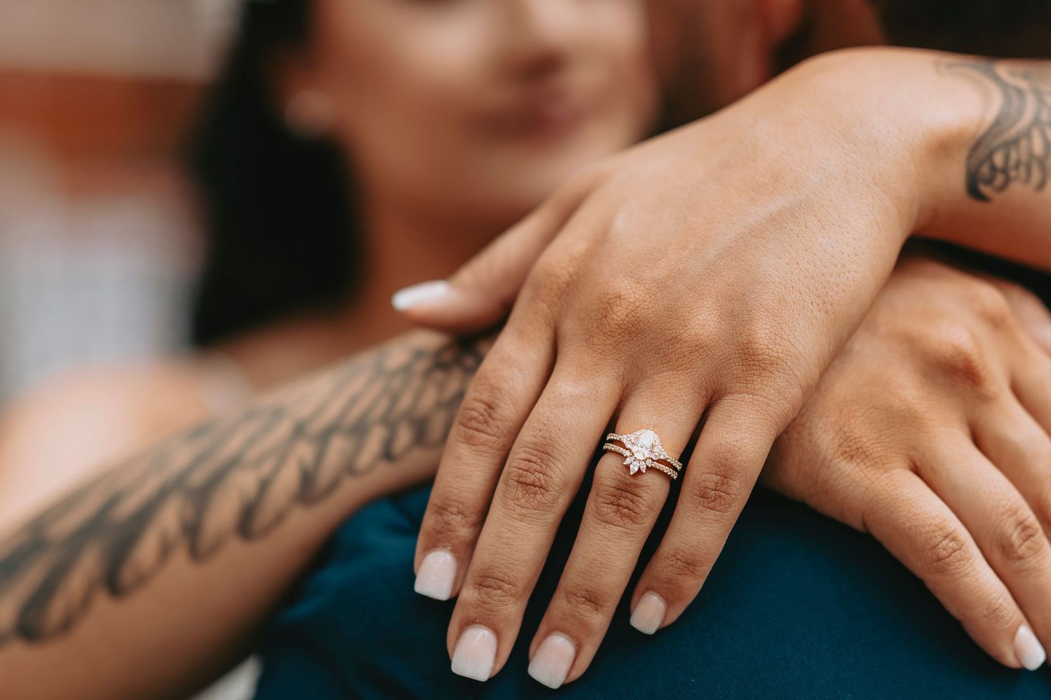 Close-up shot of tattooed hands with engagement ring and white manicure.
