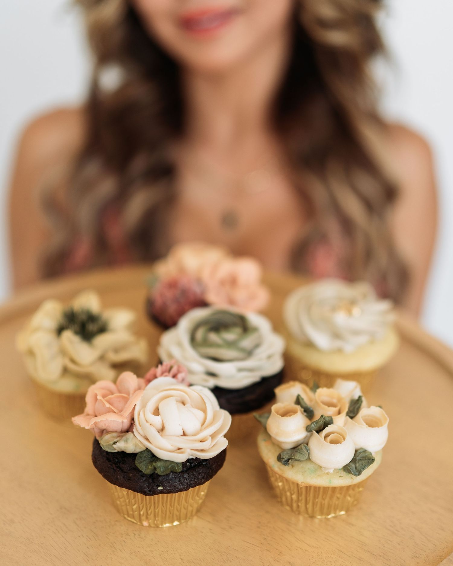 Beautiful cupcakes decorated with delicate floral designs arranged on a wooden surface, surrounded by soft bokeh effect.