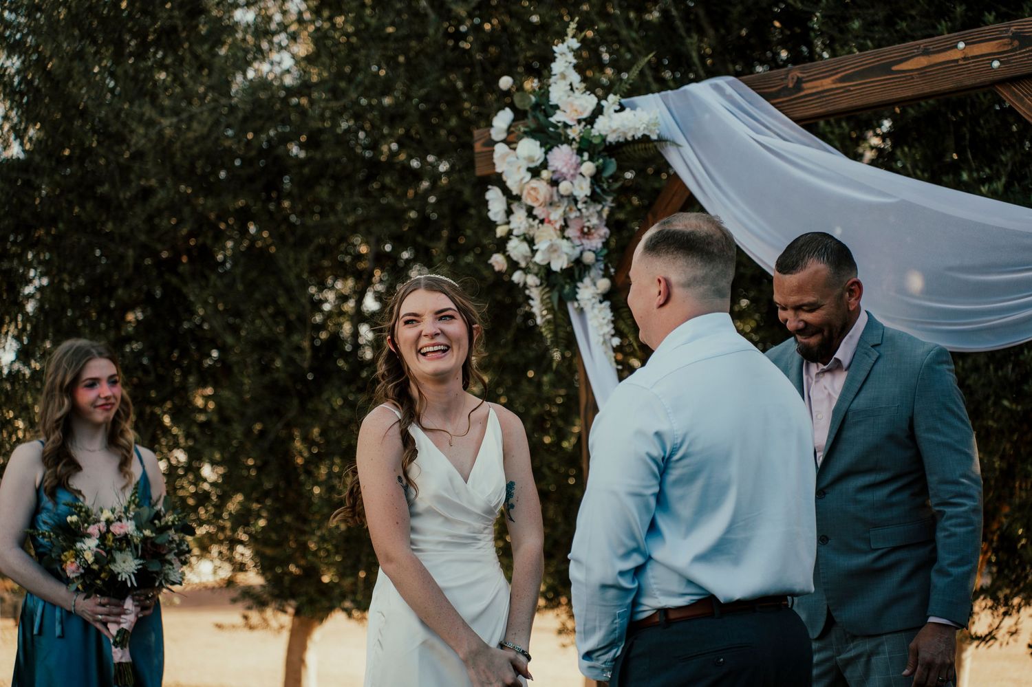 Wedding party members interact during an outdoor ceremony in natural lighting.