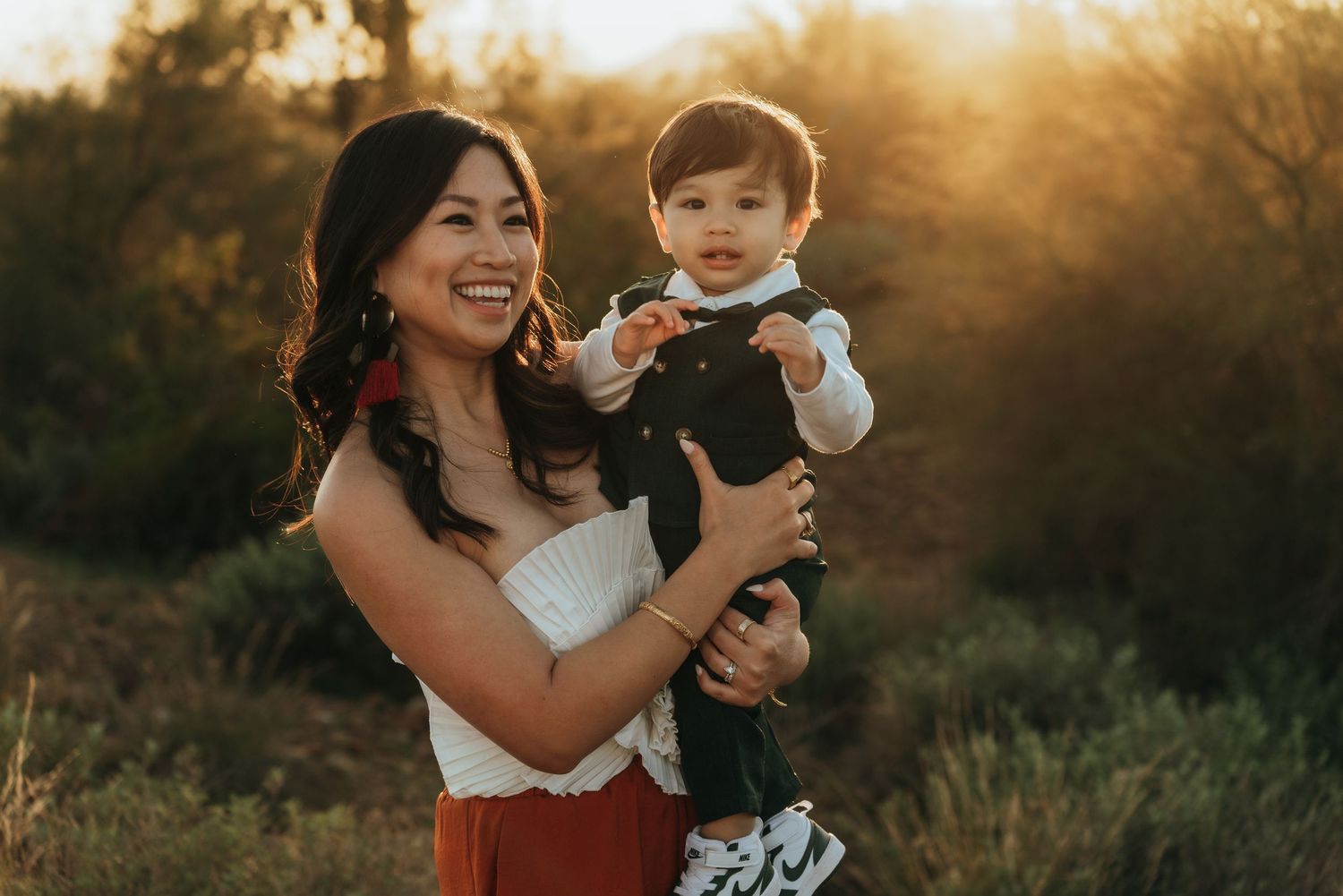 A joyful moment captured at sunset with a small child in formal attire being held against a golden backlit background.