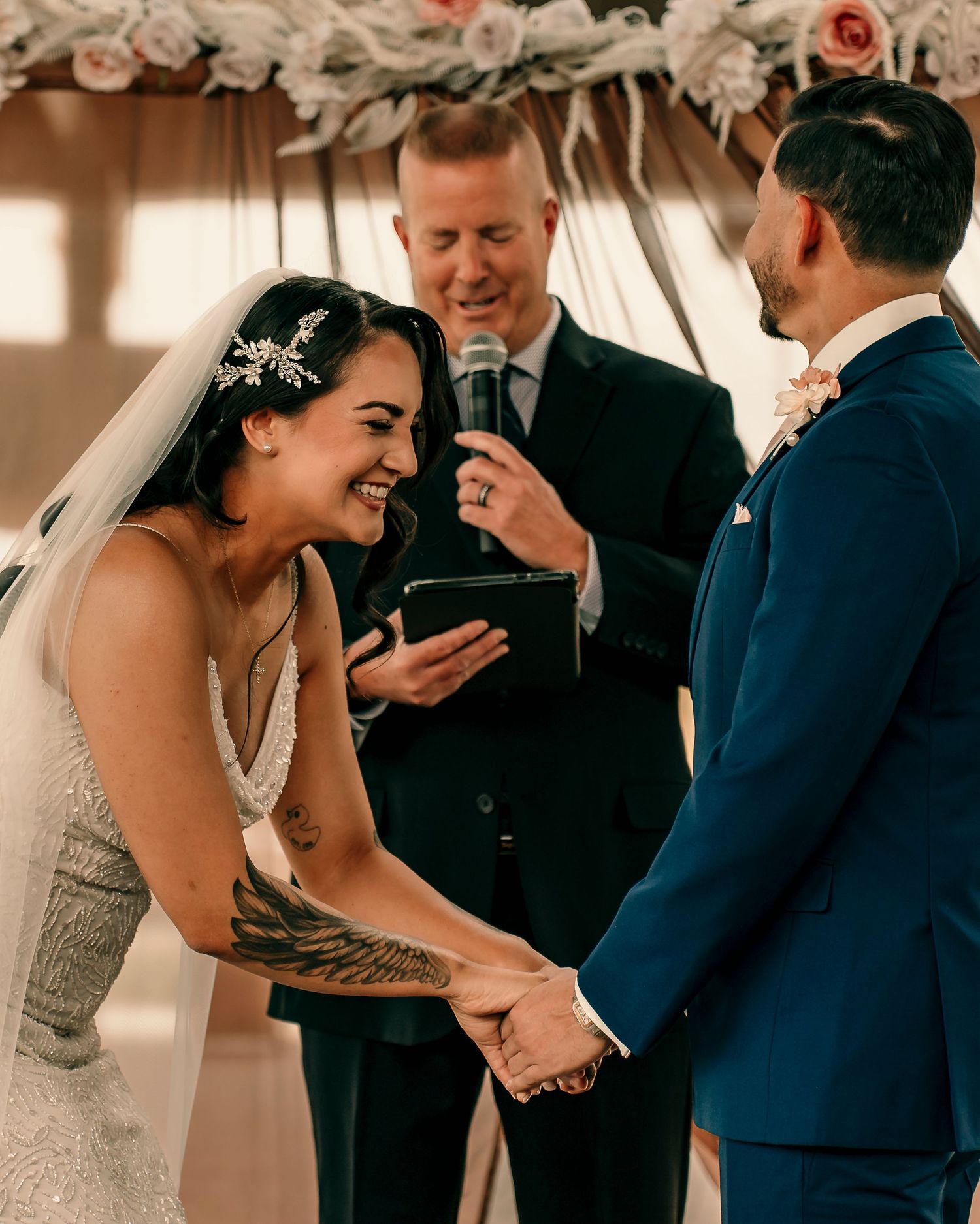 A joyful moment during a wedding ceremony as guests laugh under a floral arch.