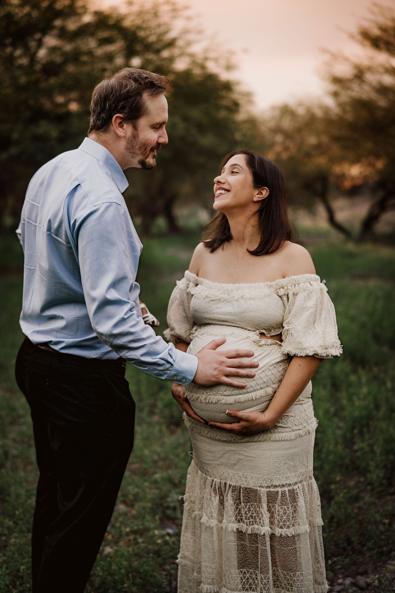 An intimate maternity moment captured outdoors with a couple in elegant attire.