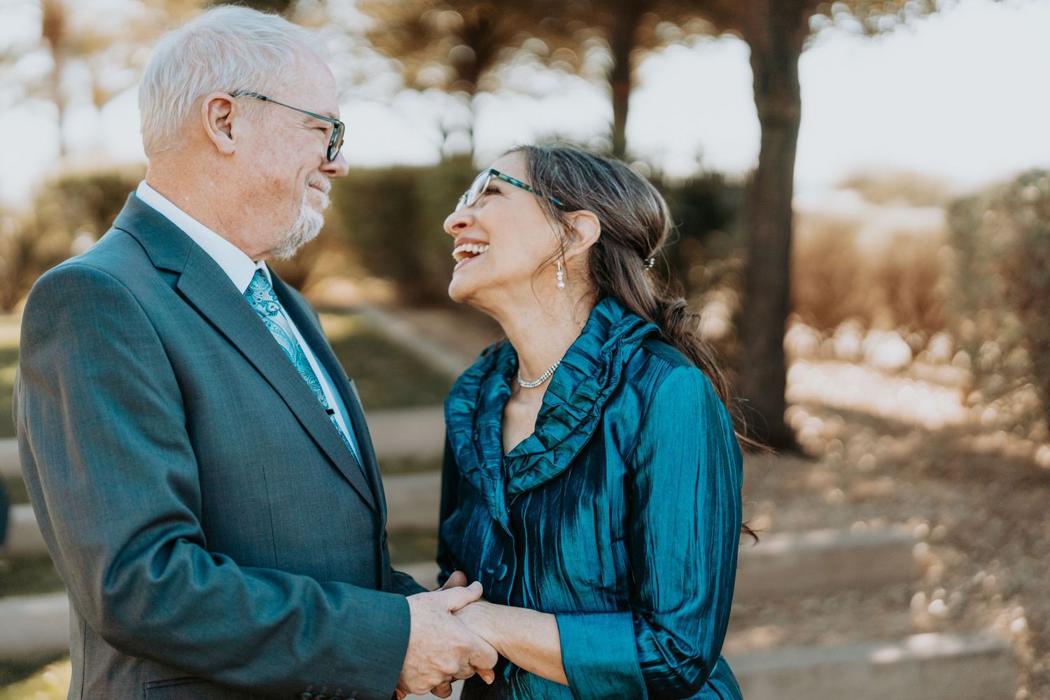 Senior couple in formal wear laughing together during outdoor photoshoot.