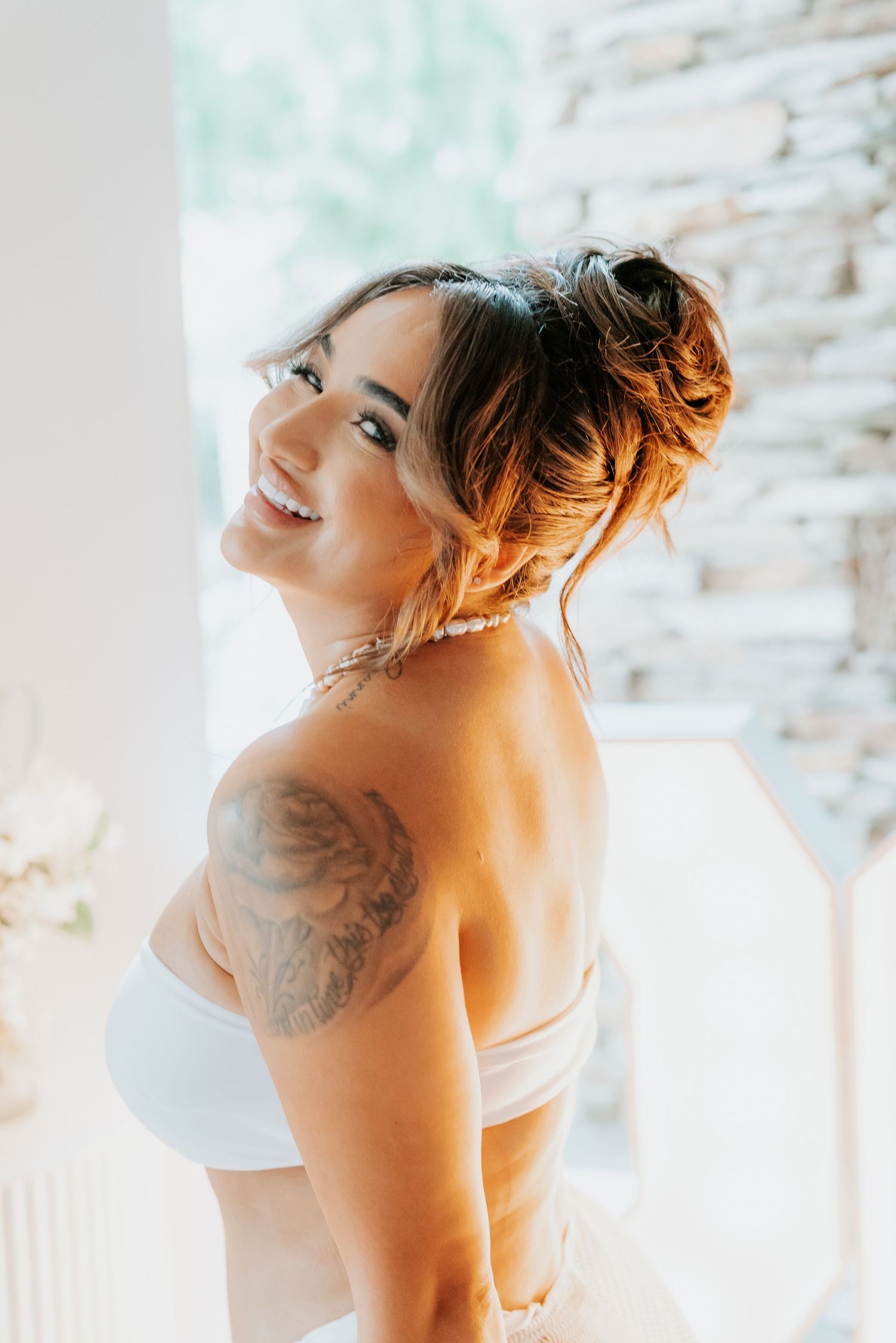 Woman in white top showing shoulder tattoo with updo hairstyle.