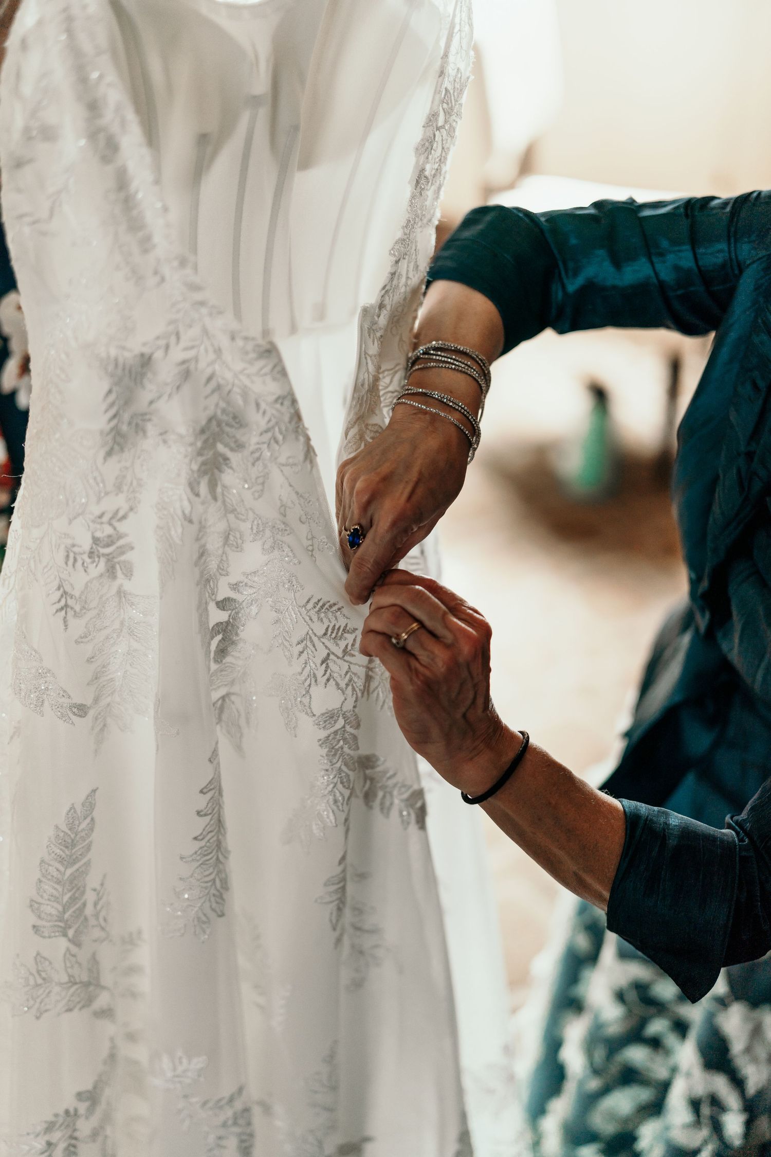 Detailed shots of hands making final adjustments to a white lace wedding gown.