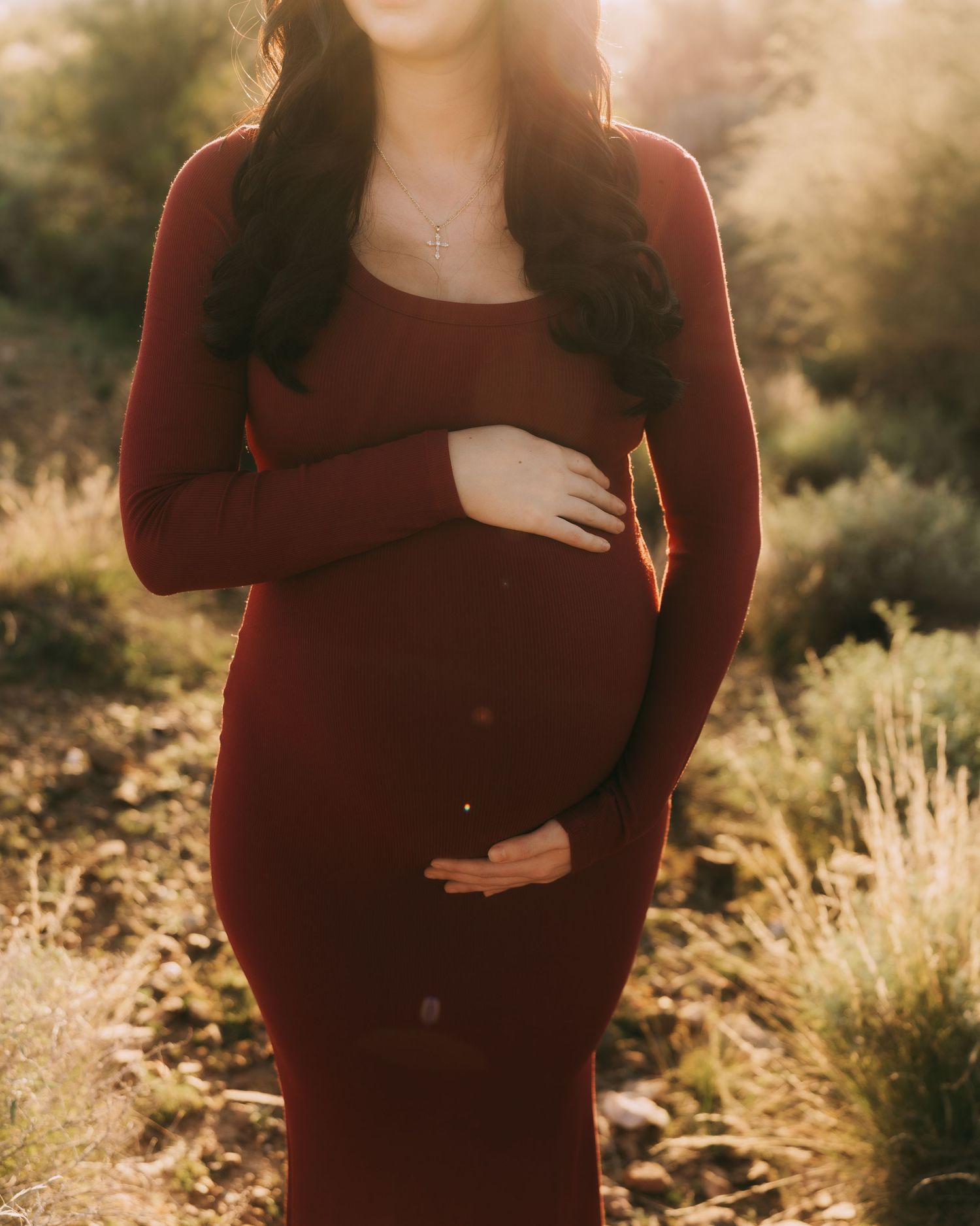 Person in burgundy sweater poses against golden sunlit foliage during autumn sunset photoshoot.