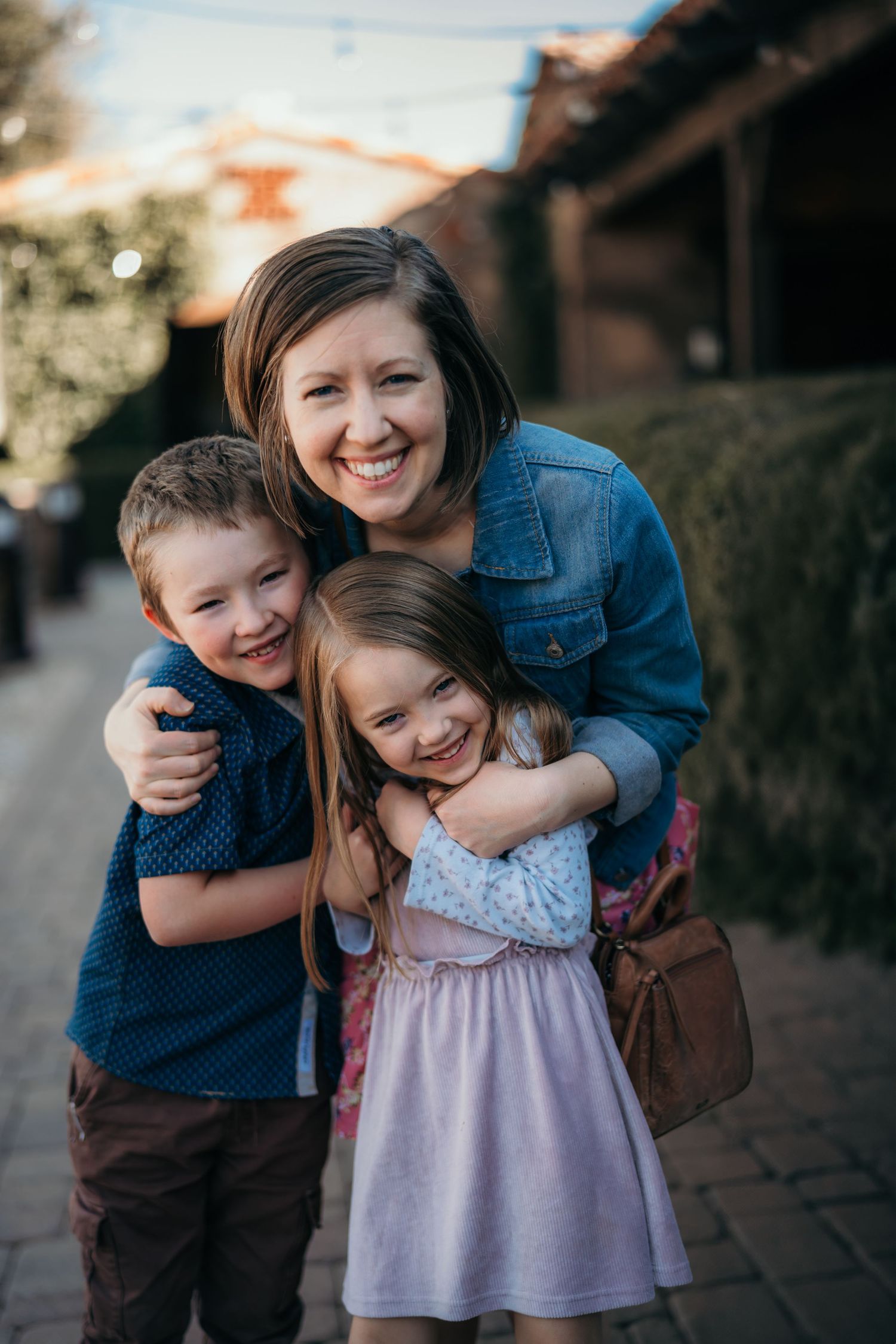 Joyful family moment captured outdoors with siblings and parent sharing embraces and laughter.