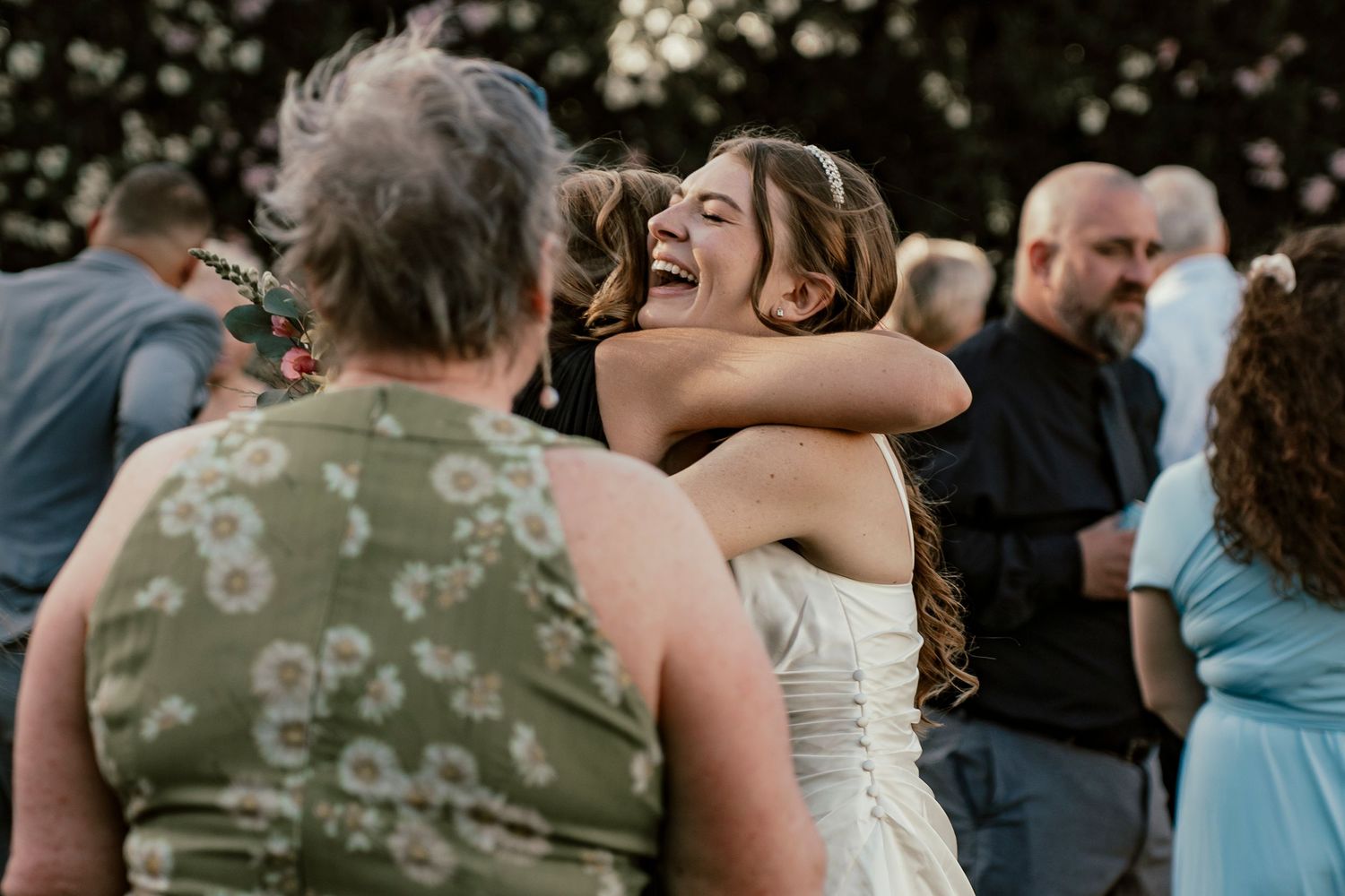 A joyful embrace captured during an outdoor celebration with guests in the background.