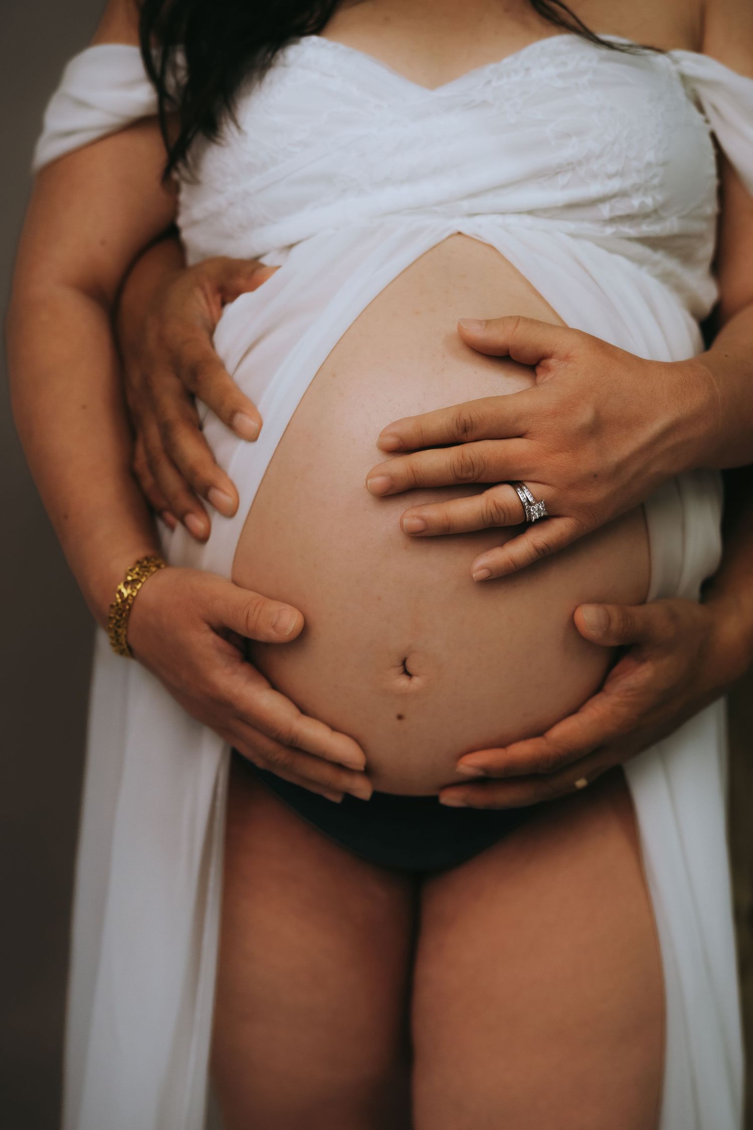 A series of five photos showing the progression of a growing pregnant belly wrapped in white fabric with hands cradling it.