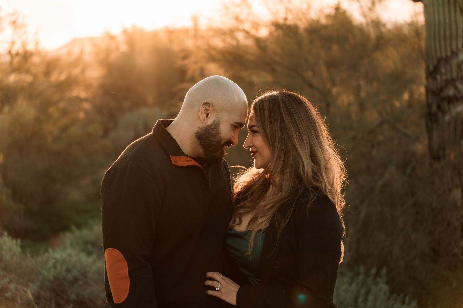 A couple embraces in silhouette against a warm sunset sky with trees in the background.