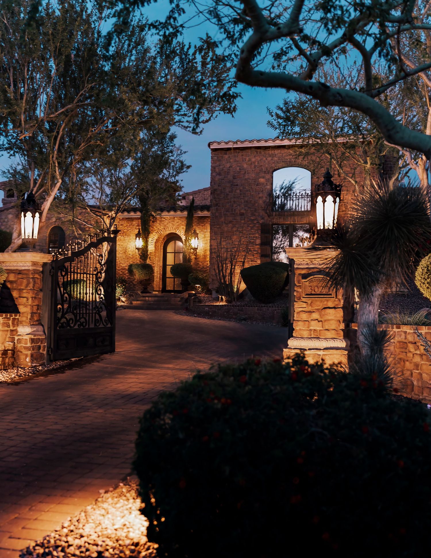 Stone pathway illuminated by warm landscape lighting leads through garden with glowing lanterns at dusk.